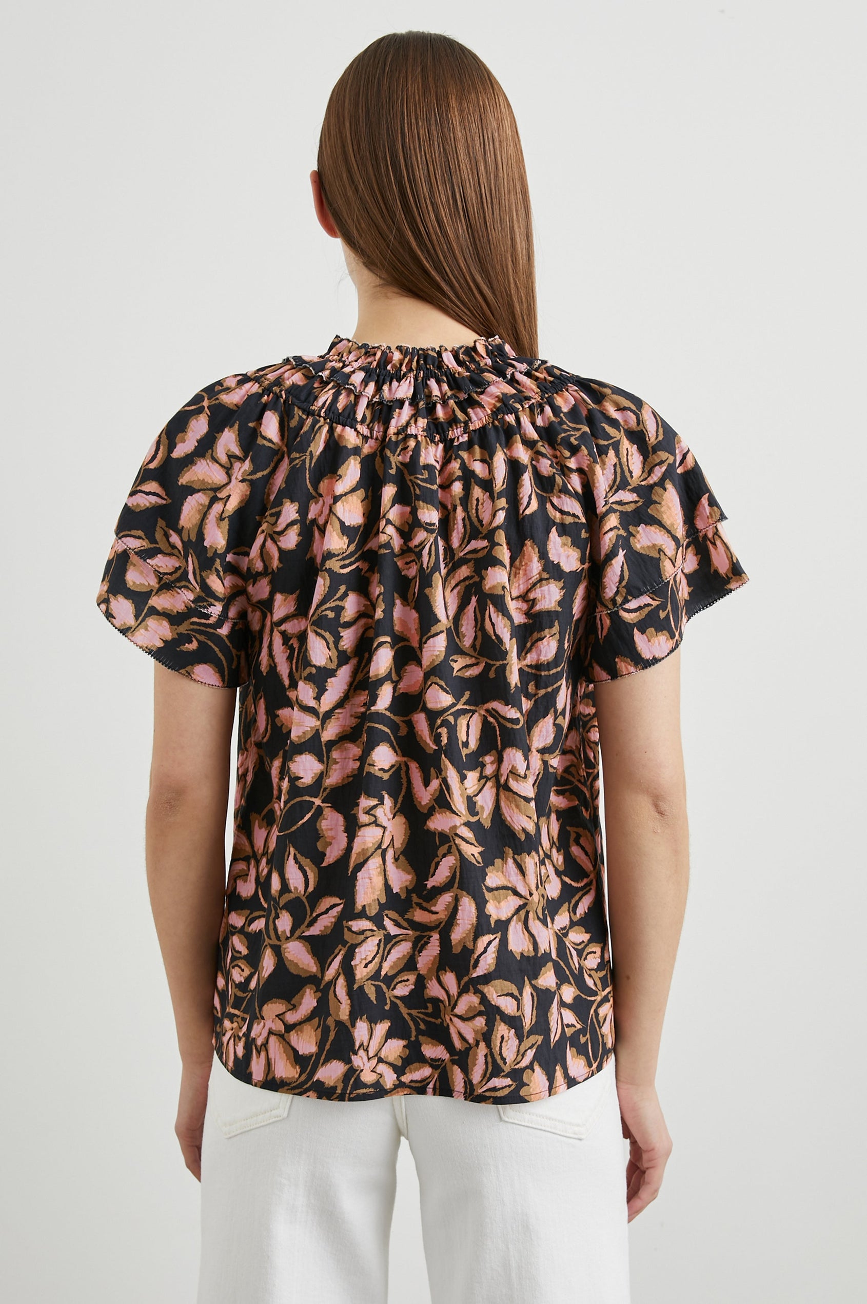 Kamila Short-Sleeve Top with Ruffled Sleeves, Deep V neck, and a Shirred Collar with a button in Jasmine Colorway, with pink and brown flowers on black - Back View Featured on Model