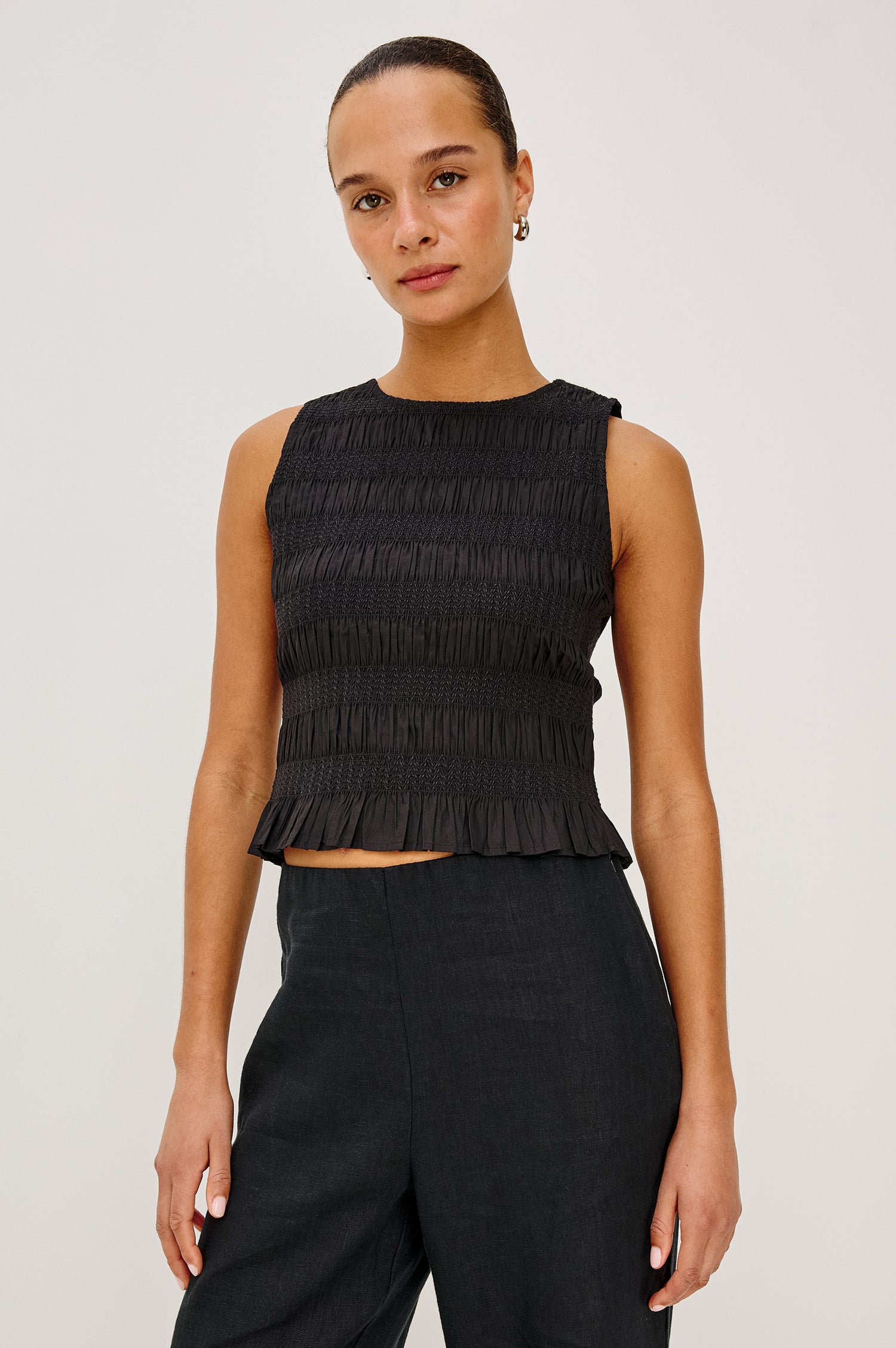 Kane Sleeveless Fitted Top in Cotton With Diamond Smocking All Over, High Boat Neckline, and Flared Ruffle Hem in Black Colorway - Upper Body Front View Featured on Model