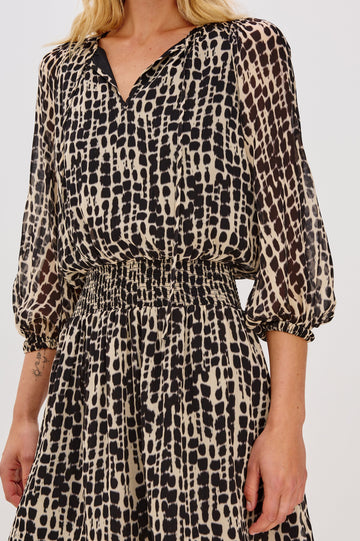 Printed dress with a tiered skirt and smocked detailing at the shoulders and waist. The dress includes a front tie closure for an adjustable neckline. Close Up View on Model.