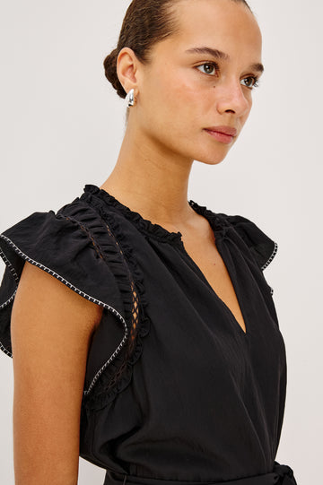 Katia Mini Dress in Textured Poplin With Shirring, Lace, and Ruffle Trim at Shoulders, Flutter Sleeves With Contrast Stitching, Adjustable Belted Ties, and Fully Lined Skirt in Black Colorway - Upper Body Close Up Front View Featured on Model