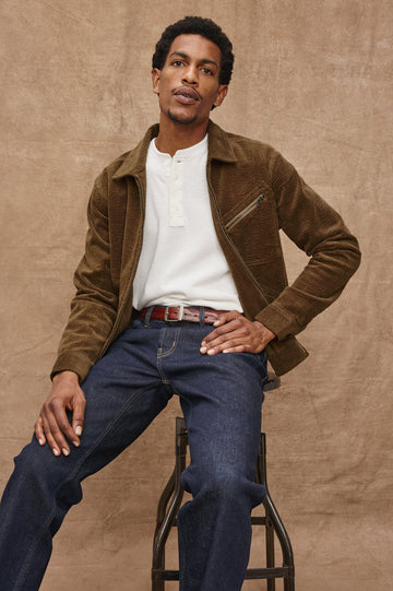 Ketter Zip Up Jacket with Two Curved Front Patch Pockets, a Diagonally Zippered Chest Patch Pocket and Adjustable Button Straps on the Hem in Chicory Colorway, a Warm Brown with Non Contrast Collar - Front Seated View Featured on Model.