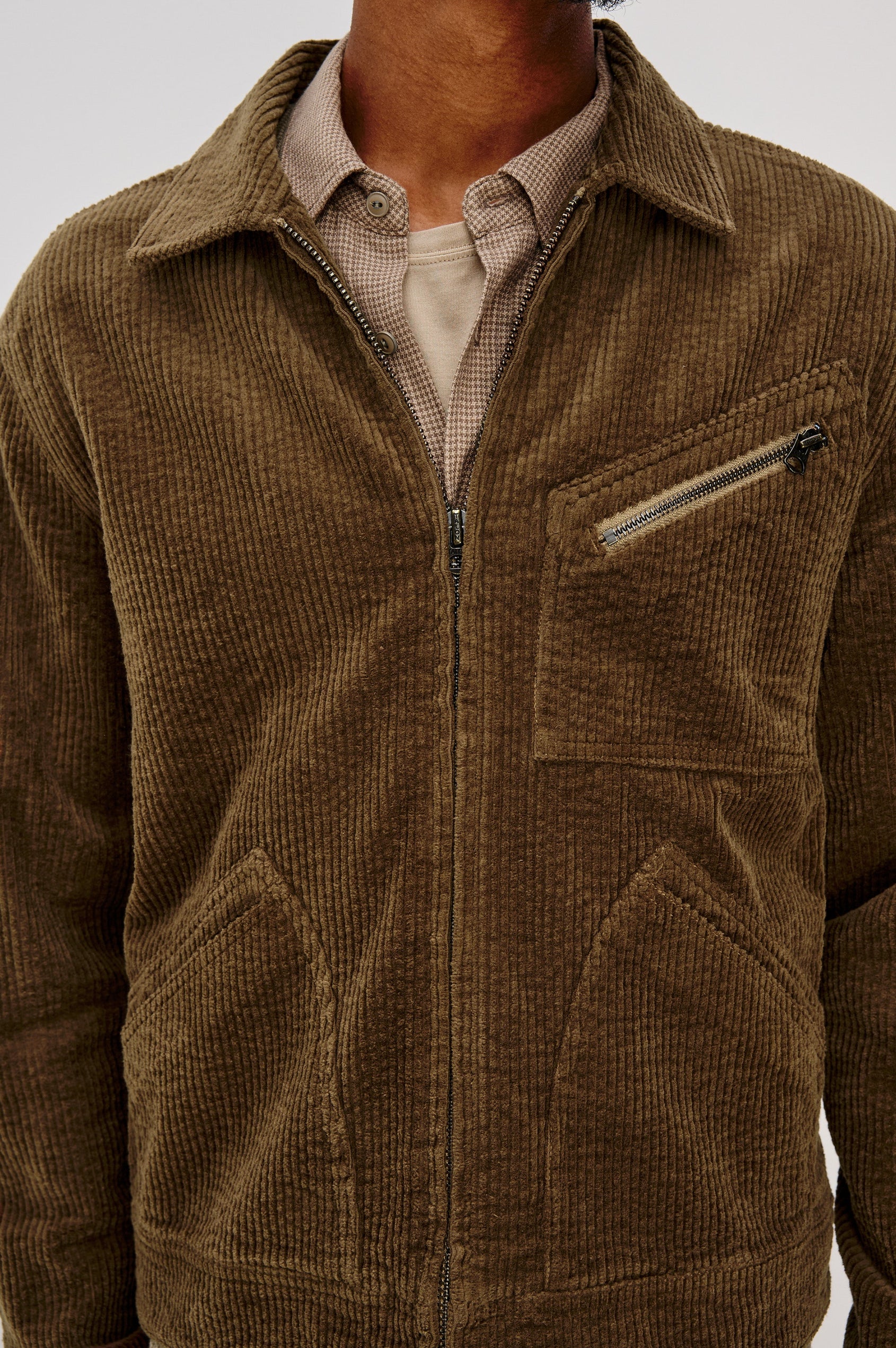 Ketter Zip Up Jacket with Two Curved Front Patch Pockets, a Diagonally Zippered Chest Patch Pocket and Adjustable Button Straps on the Hem in Chicory Colorway, a Warm Brown with Non Contrast Collar - Front Detail View Featured on Model.