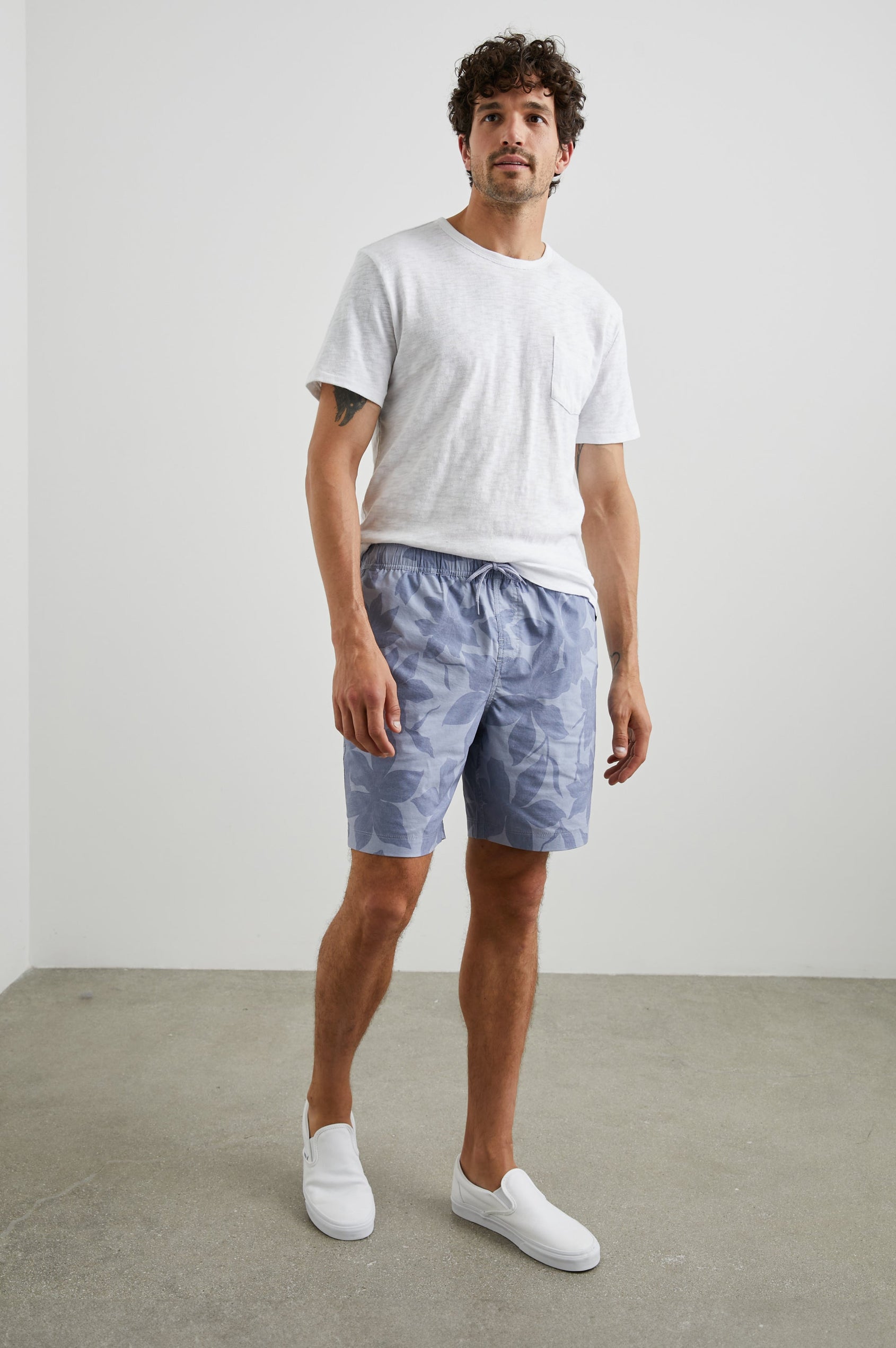 Kian Swim Shorts with an Elastic Drawstring Waistband, Two Front Pockets and a Back Button Flap Pocket in Garden Sands Orchid Colorway, Blue Orchids on Light Blue - Front Full Body View Featured on Model