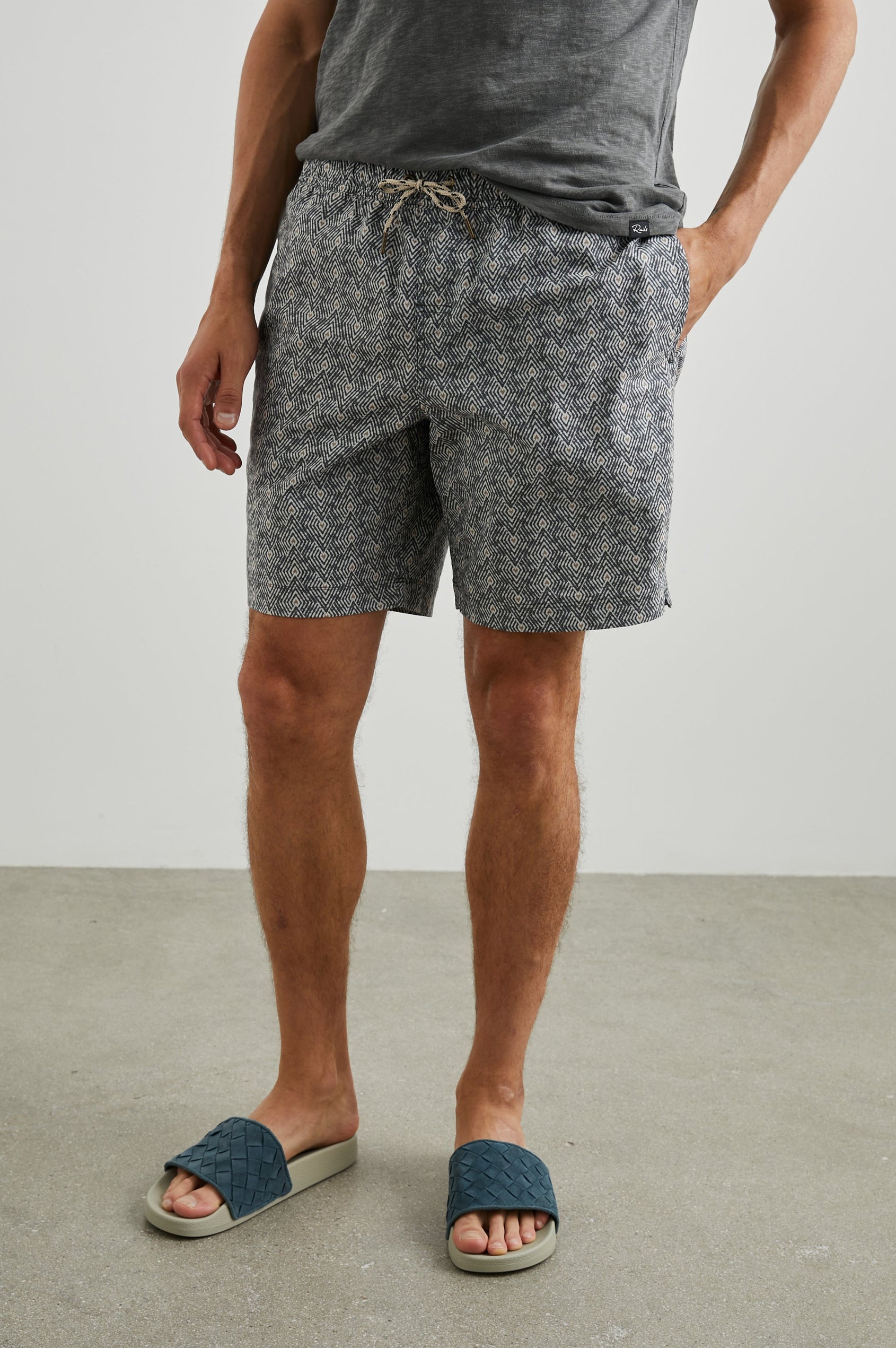 Kian Swim Shorts with an Elastic Drawstring Waistband, Two Front Pockets and a Back Button Flap Pocket in Tribal Batik Celestial Colorway, Geometric patten in Black, White and tan - Front View Featured on Model