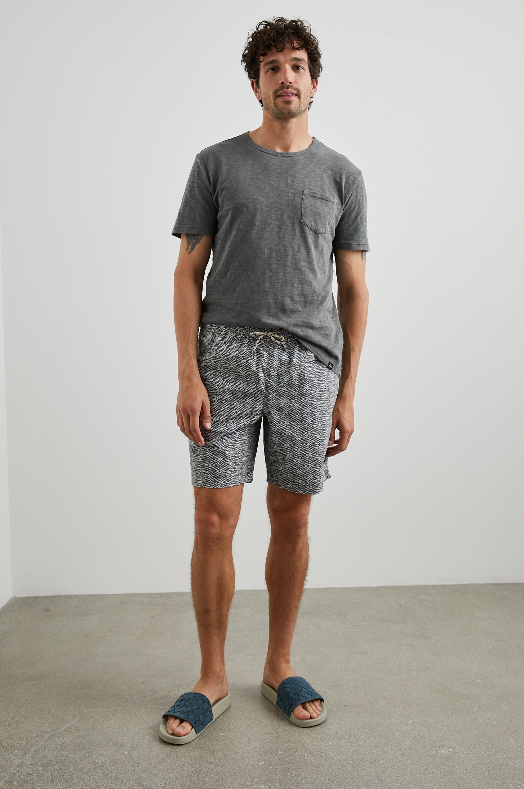 Kian Swim Shorts with an Elastic Drawstring Waistband, Two Front Pockets and a Back Button Flap Pocket in Tribal Batik Celestial Colorway, Geometric patten in Black, White and tan - Front Full Body View Featured on Model