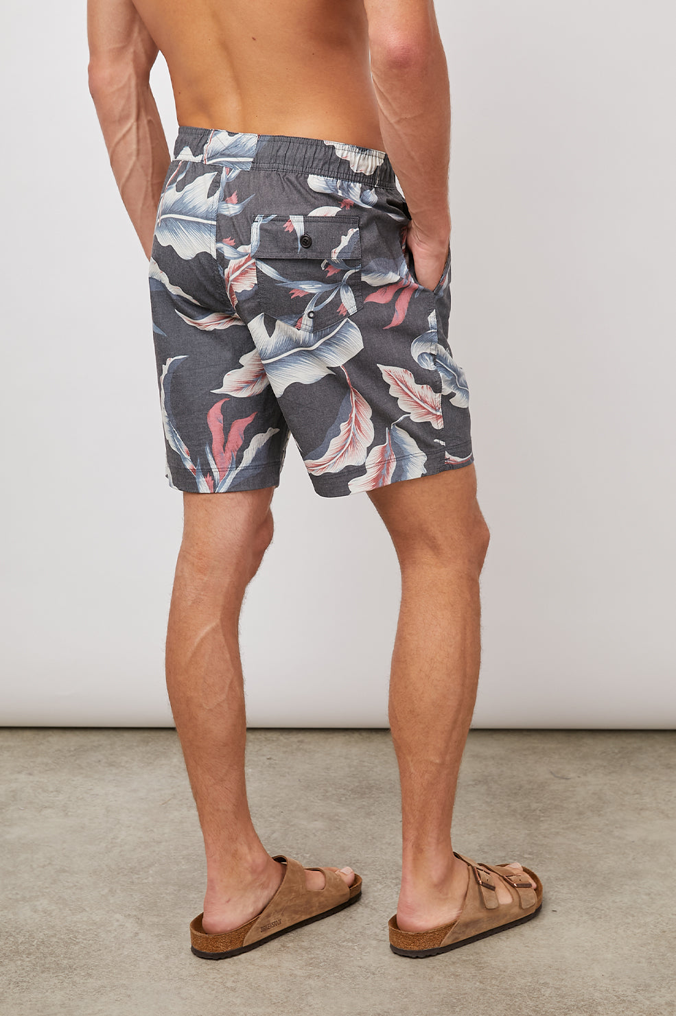 Kian Swim Shorts with an Elastic Drawstring Waistband, Two Front Pockets and a Back Button Flap Pocket in Paradise Nights Colorway, a Floral Print in Pinks, Blues and White on Black - Back View Featured on Model