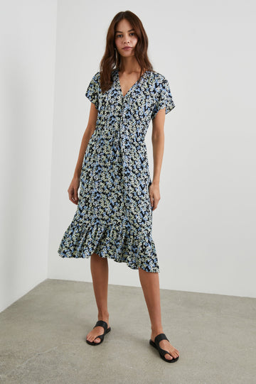 Kiki Short Sleeve Midi Dress with a V Neck, Buttons Down the Front Bodice, a Drawstring Waist and Ruffles at the Hem in Midnight Meadow Floral Colorway, Blue and Cream Flowers on Black - Front Full Body View Featured on Model 