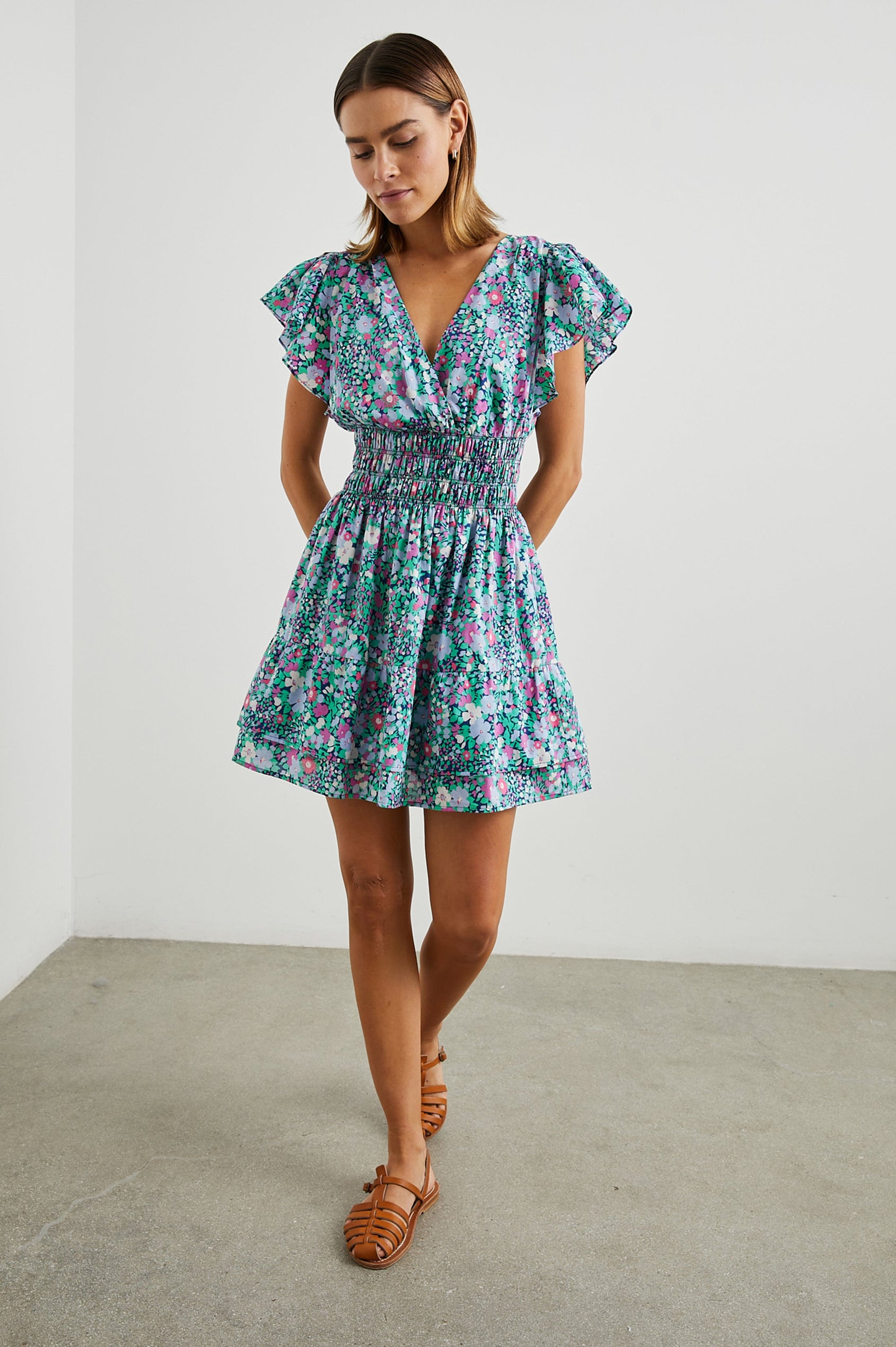 Kimora Above-Knee Dress with Flutter Sleeves, a V Neckline, a Cinched Waist and a Tiered Skirt in Navy Leilani Floral Colorway with flowers in pinks, purples and greens - Front Full Body View Featured on Model