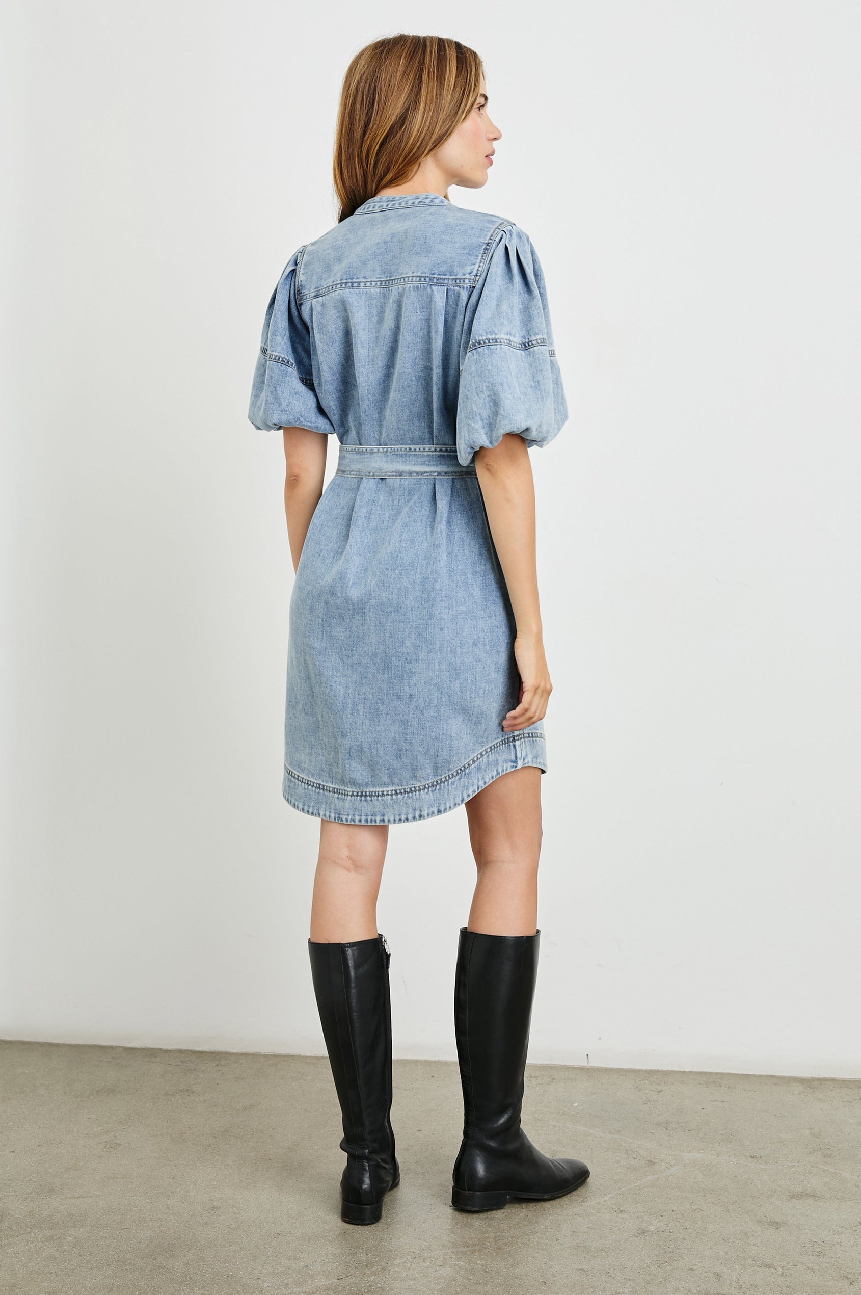Kingsley Denim Mini Dress with Elbow-Length Puff Sleeves, a V Neck, Snaps Down the Front and a Fabric Tie Belt in Faded Indigo Colorway - Back View Featured on Model 