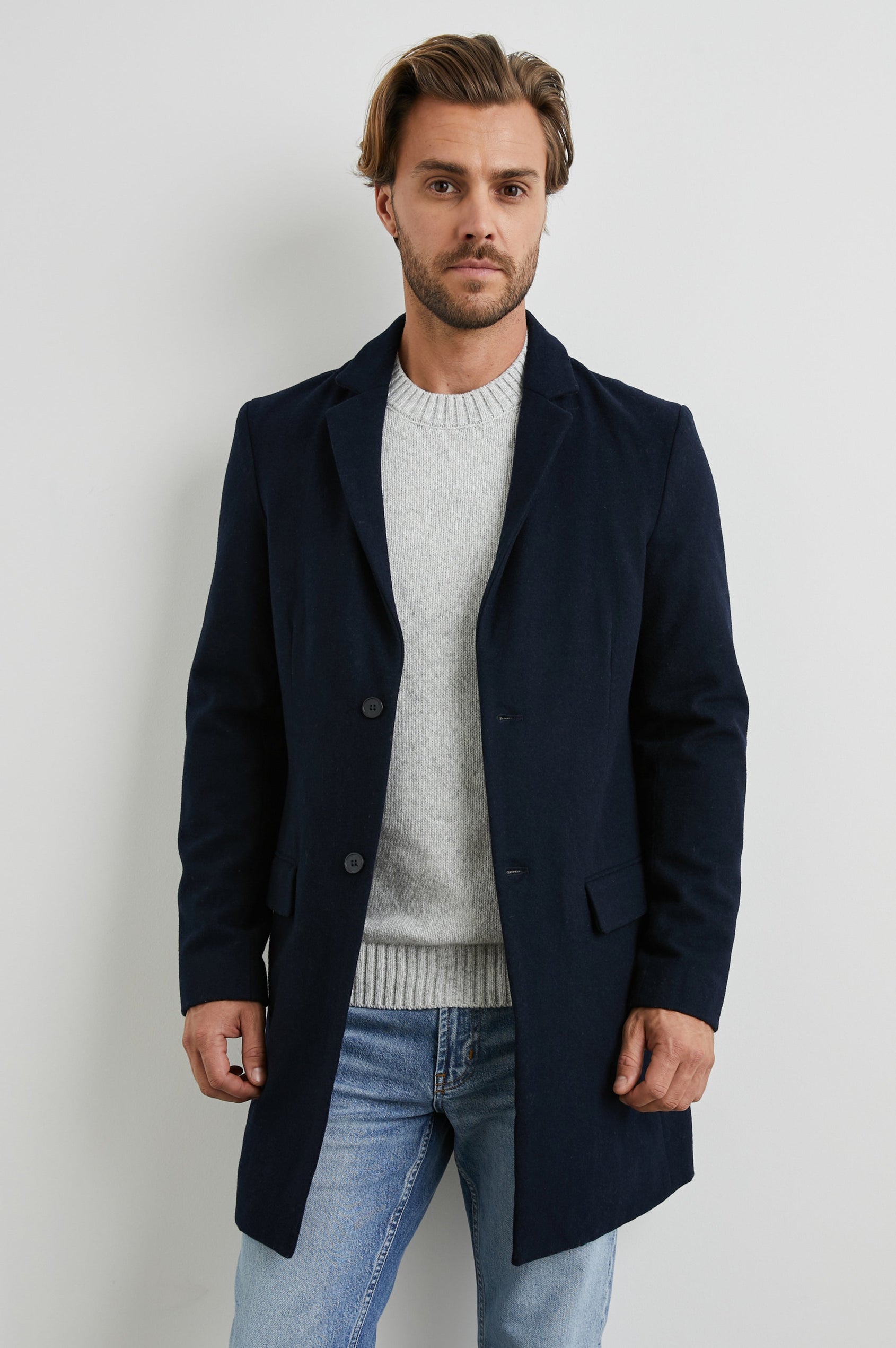 Lark Thigh-Length Coat with Two Button Closure, Notched Lapels, and Two Front Flap Pockets in Navy Colorway - Front View Featured on Model