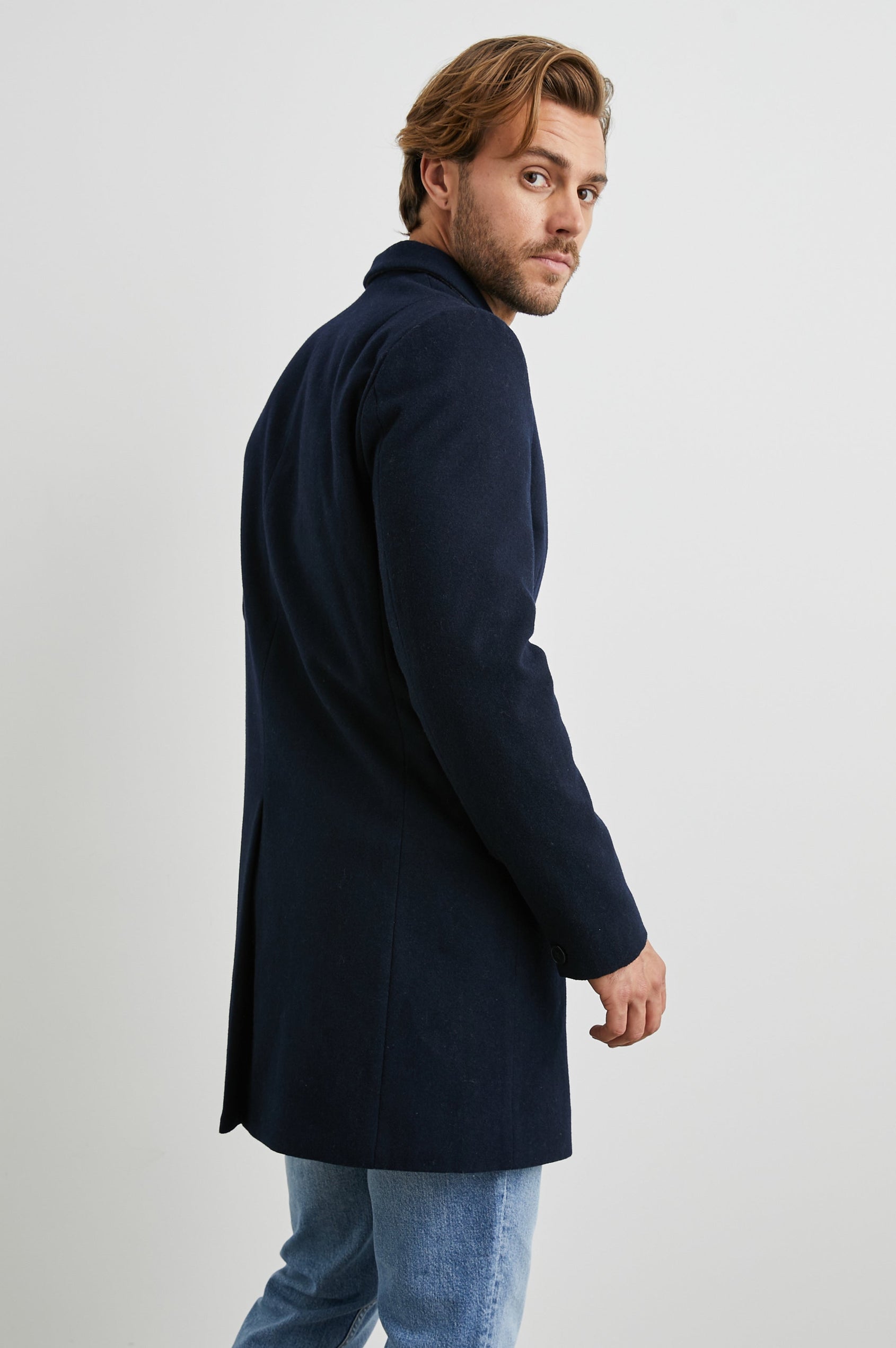 Lark Thigh-Length Coat with Two Button Closure, Notched Lapels, and Two Front Flap Pockets in Navy Colorway - Side View Featured on Model