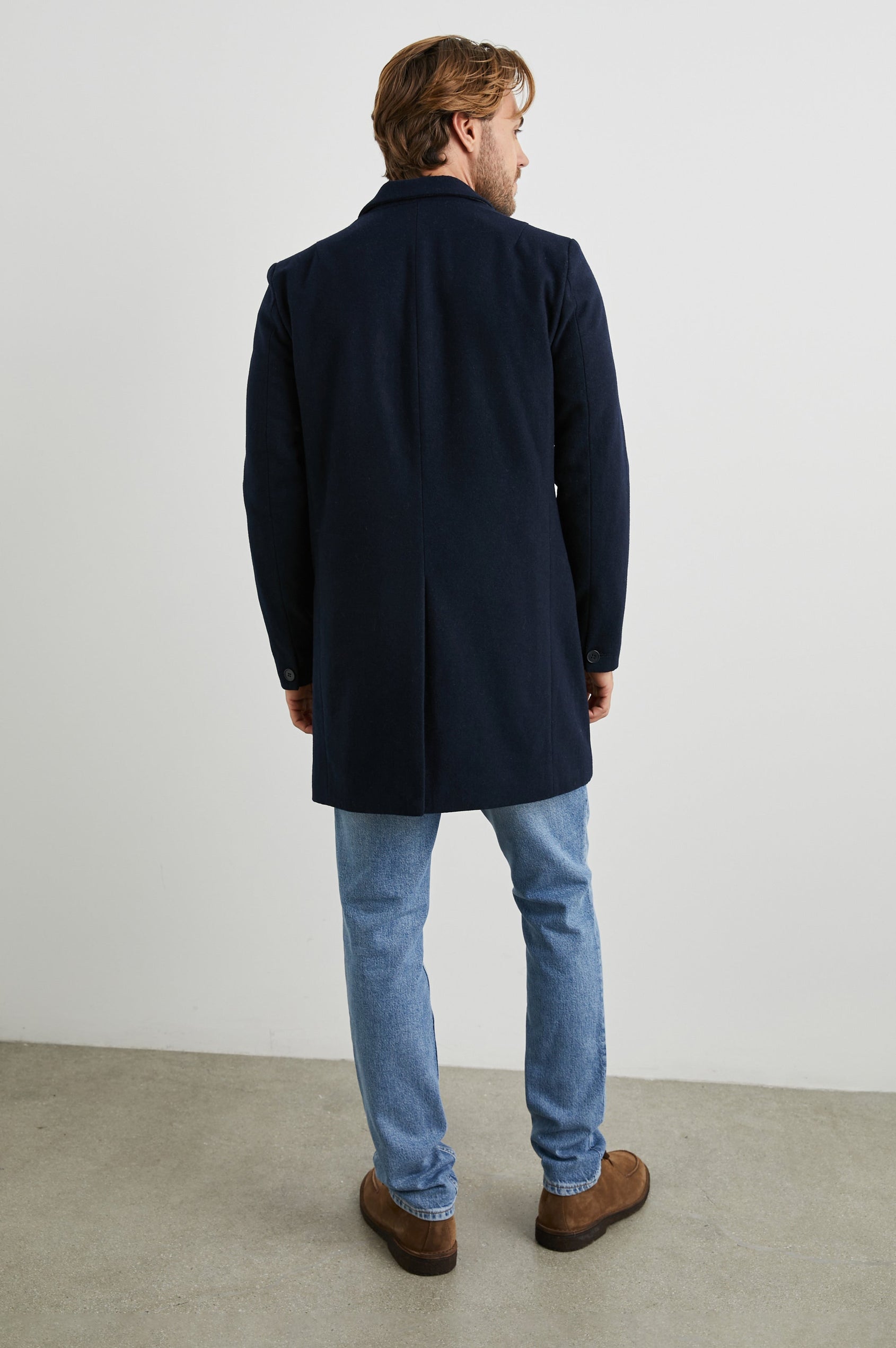 Lark Thigh-Length Coat with Two Button Closure, Notched Lapels, and Two Front Flap Pockets in Navy Colorway - Back Full Body View Featured on Model