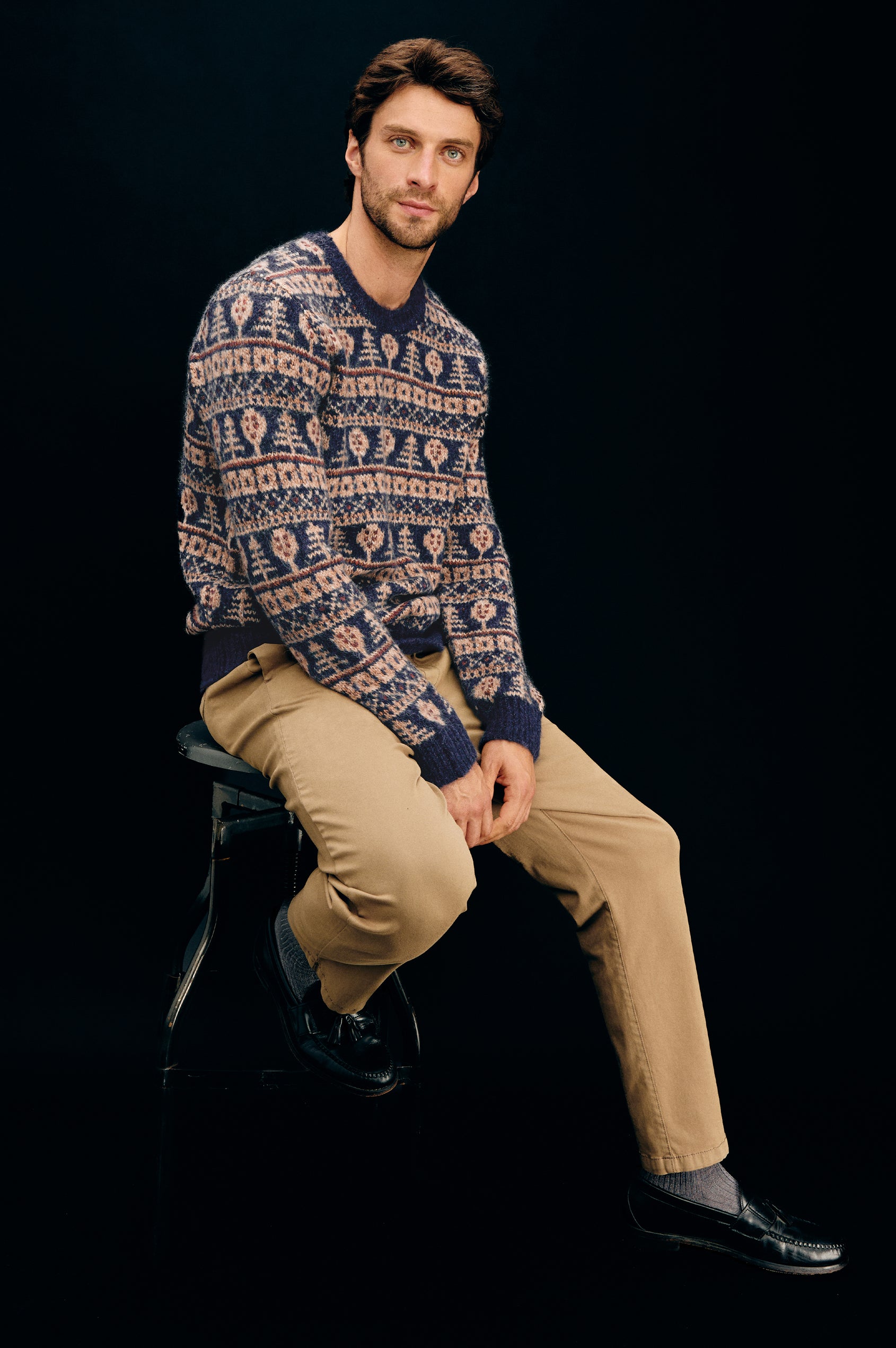 Lars is a relaxed fit crewneck sweater with long sleeves and ribbed trim, Fair Isle motifs in a merino wool blend. Side seated view featured on model.
