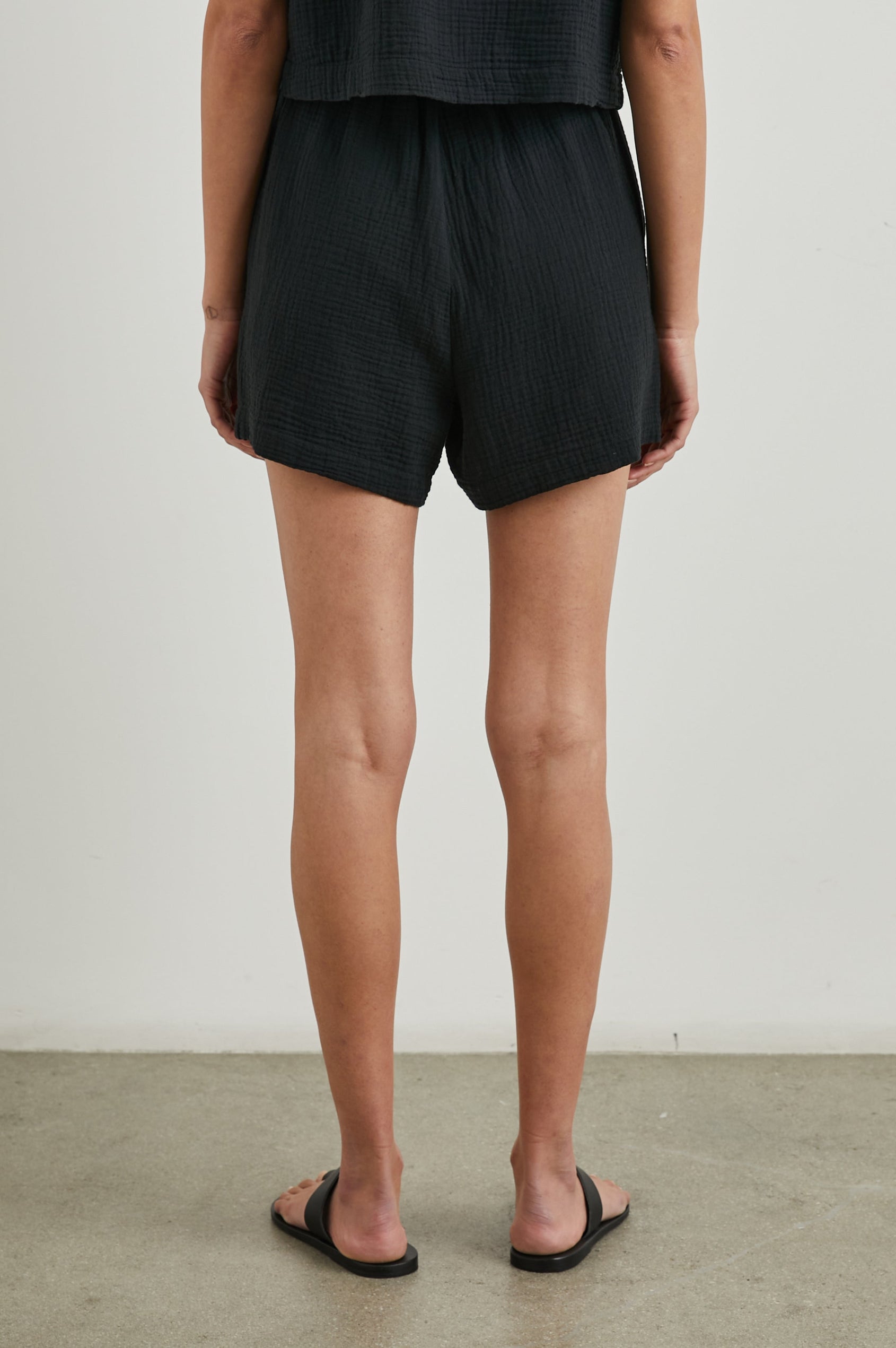 Leighton Shorts with Textured Fabric, a Smocked Elastic Waist, and Large Front Pockets in Black Colorway - Back View Featured on Model