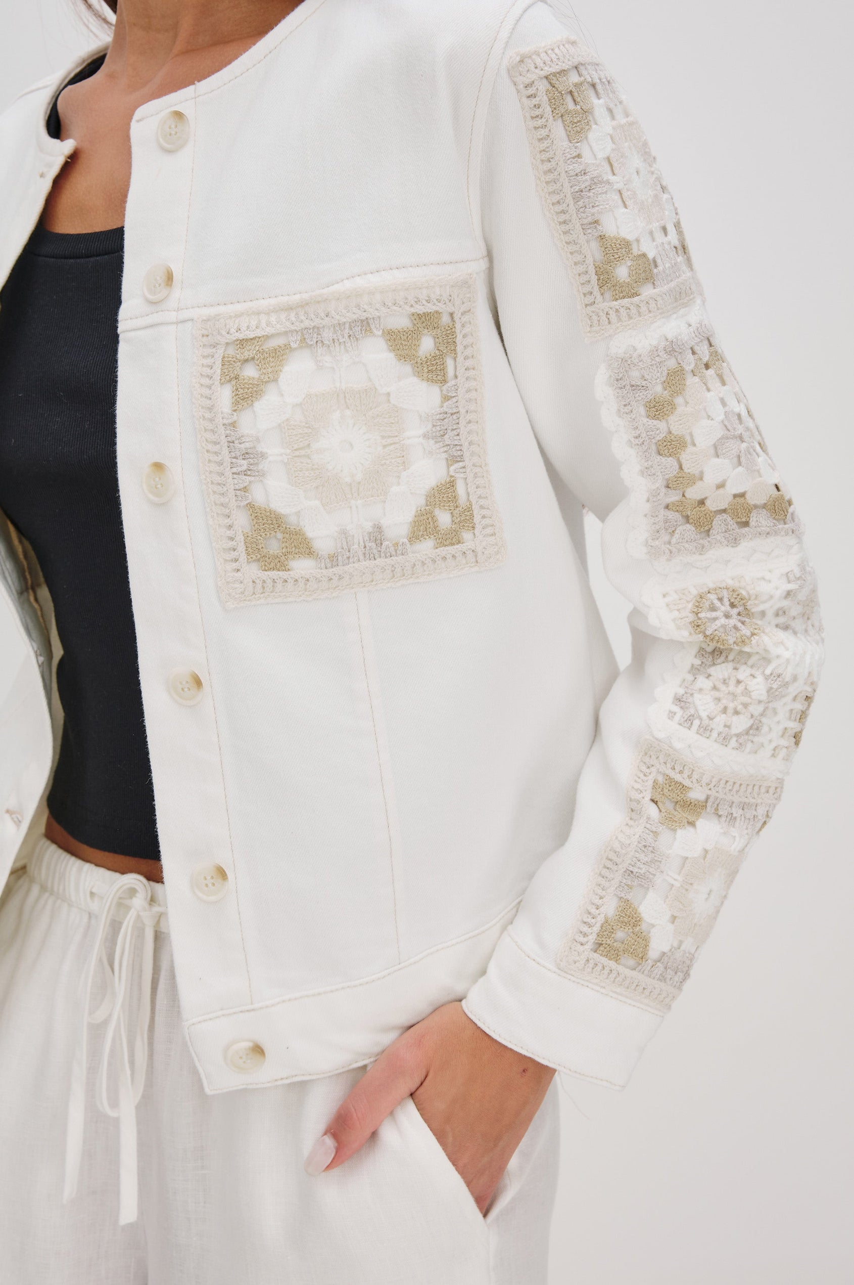 Lido collarless denim jacket with contrast embroidery details, chest pockets and embellishment buttons in vintage ecru crochet colorway. Front detail view on model.