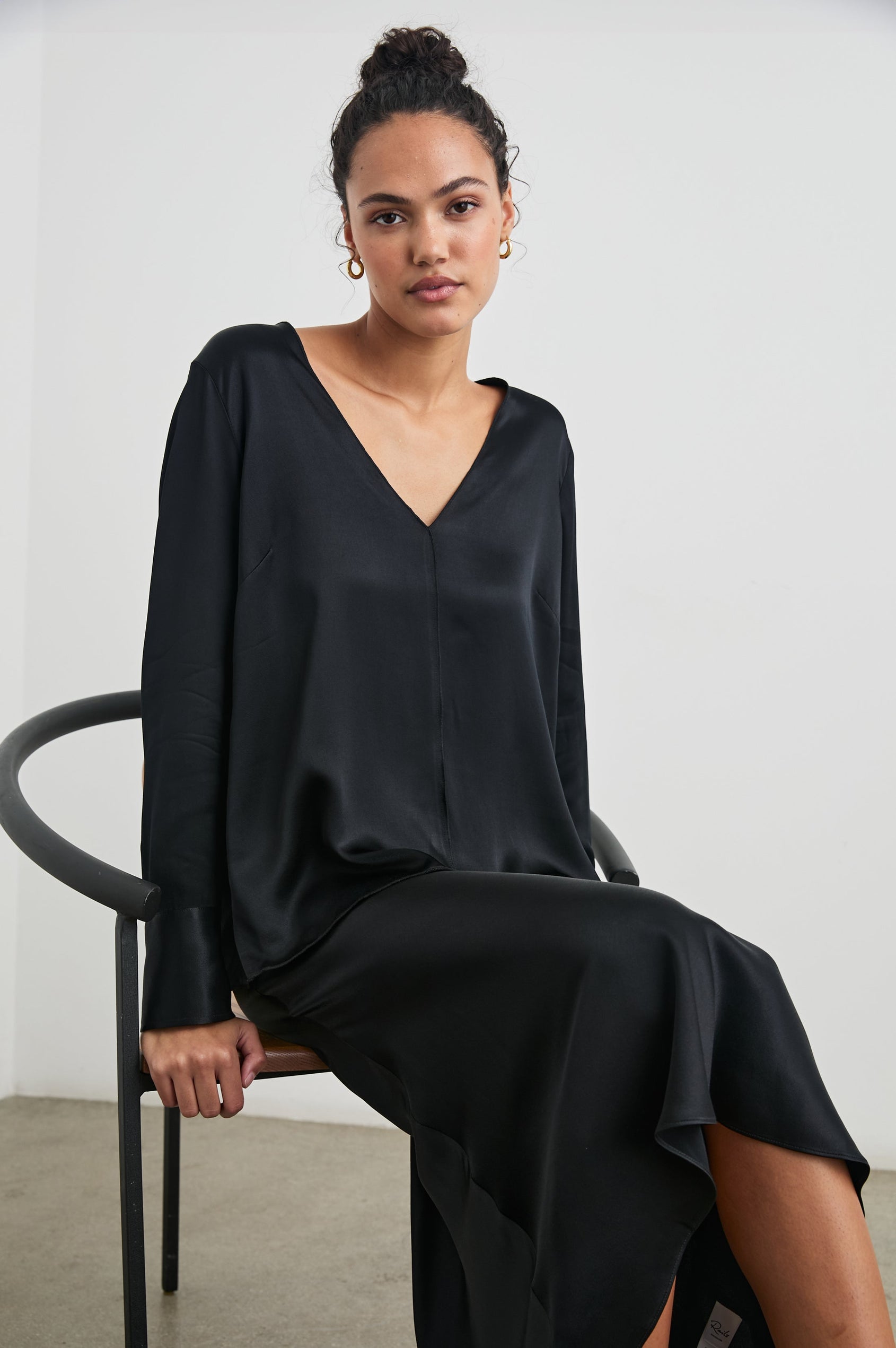Liliana Long-Sleeve Top with a V Neck, Button Cuffs and a Vertical Seam Down the Front and Back in Black Colorway - Front Full Body View Featured on Seated Model