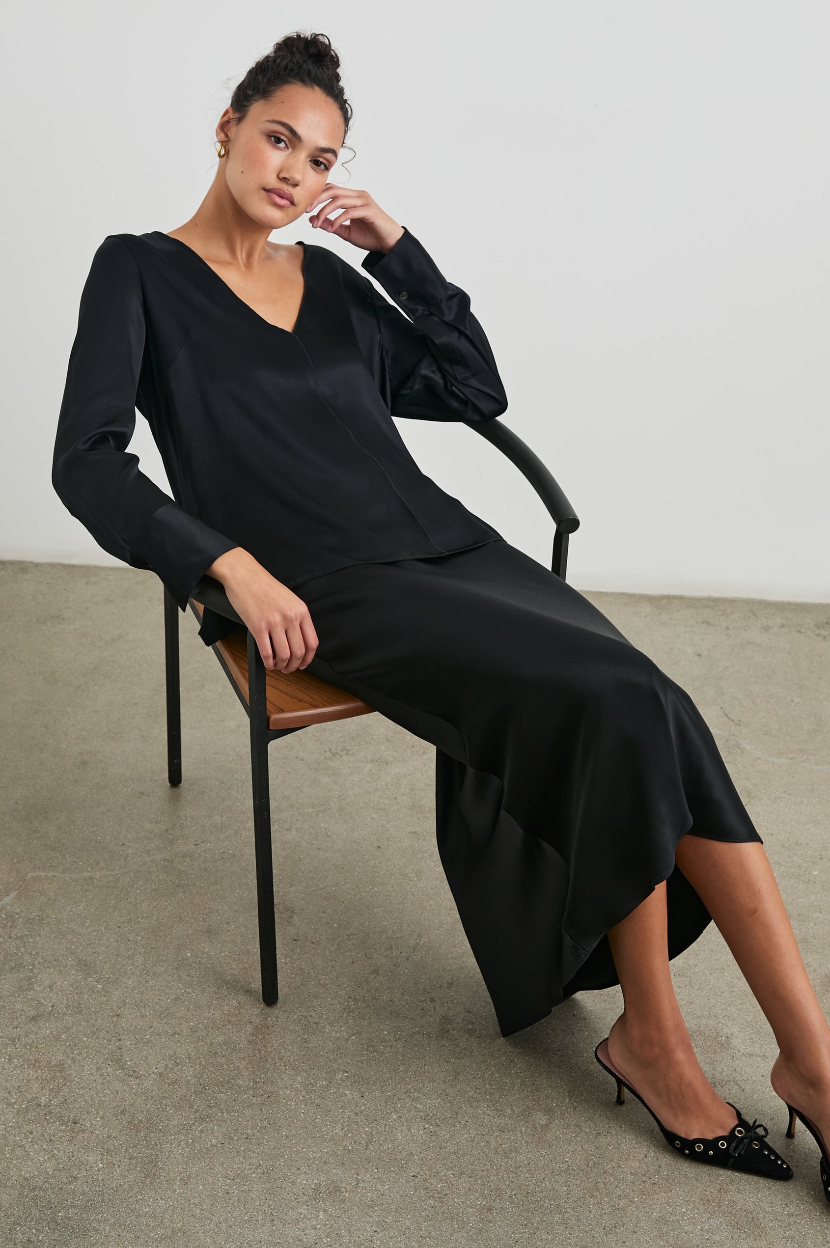 Liliana Long-Sleeve Top with a V Neck, Button Cuffs and a Vertical Seam Down the Front and Back in Black Colorway - Front Full Body View Featured on Seated Model