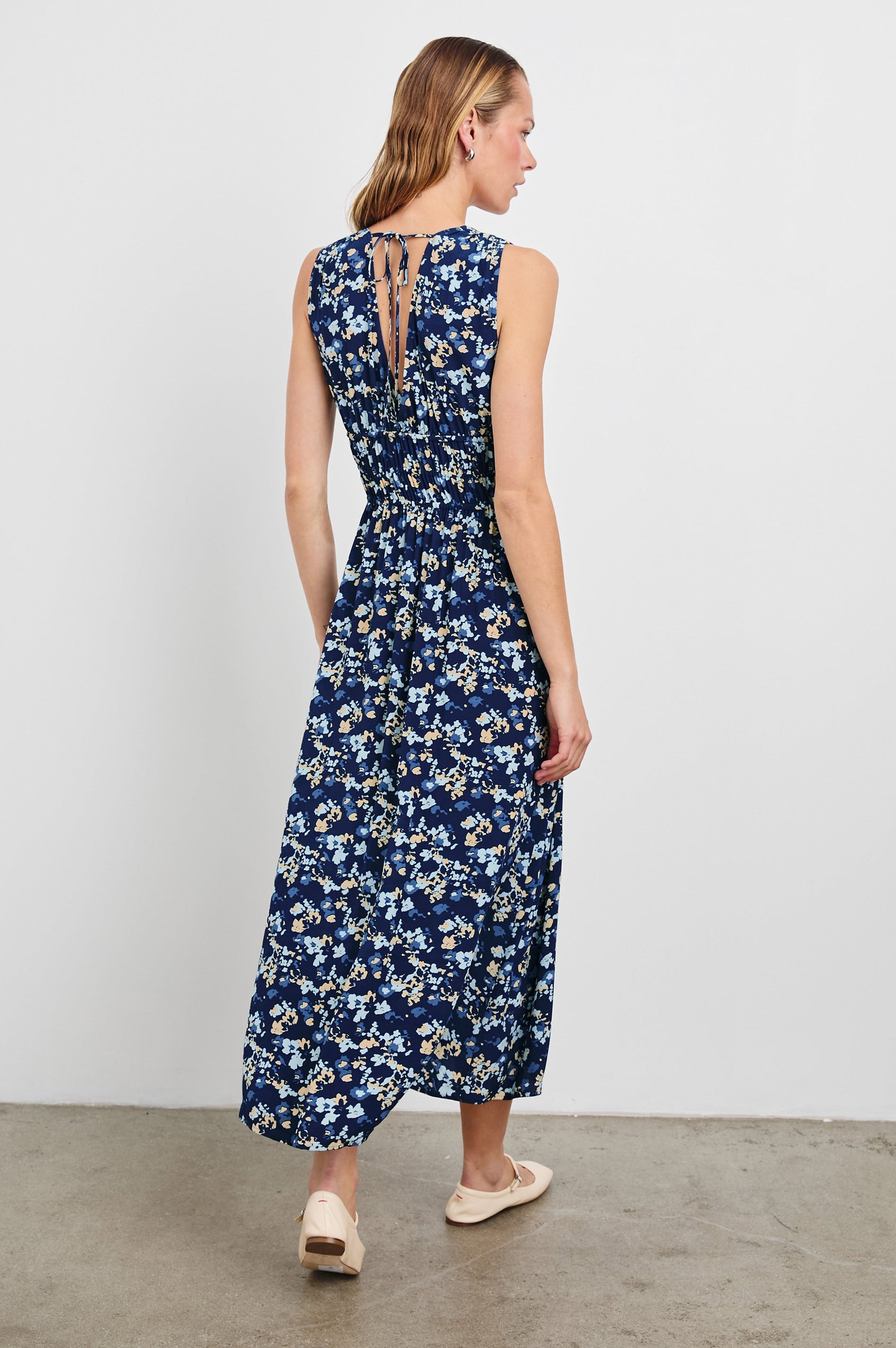 Lilith Sleeveless Midi Dress with Wide Shoulder Straps, a Deep V neck, a Cinched Waist with Drawstring, and a Back Neck Tie in Navy Flora Colorway, with flowers in creams and blues on Navy - Back Full Body View Featured on Model  