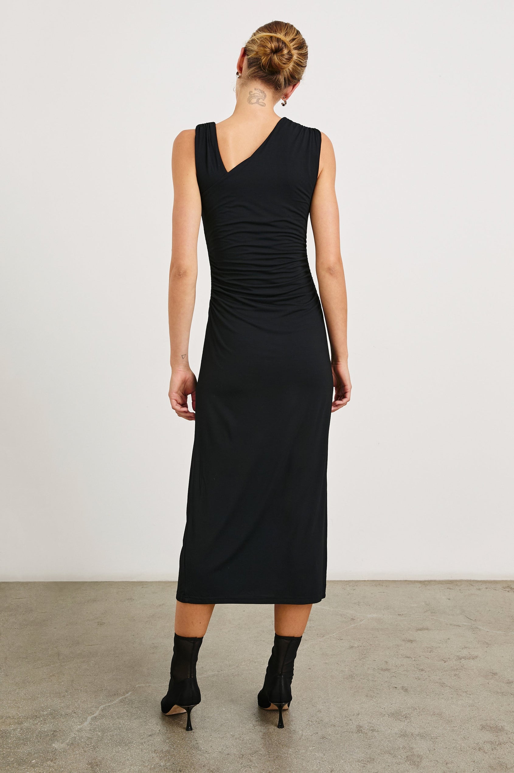Lola Sleeveless Midi Dress with Ruching Along Both Bodice Sides, a Mid-Thigh Side Slit and an Asymmetrical Neckline in Black Onyx Colorway - Back Full Body View Featured on Model
