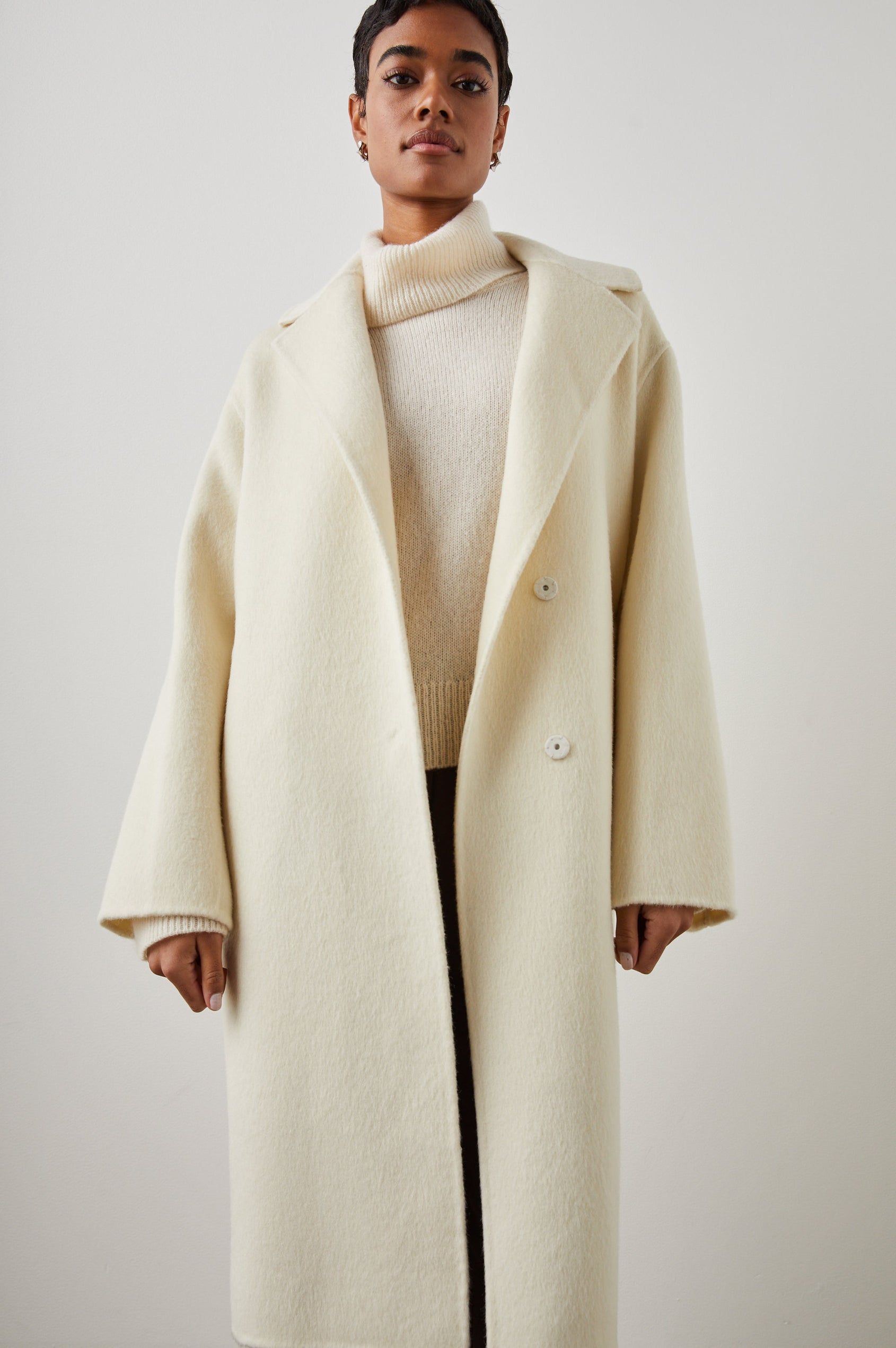 Lore Knee-Length Coat with Two Button Closure, Notched Lapels and Two Front Pockets in Ivory Colorway - Front Full Body View Featured on Model