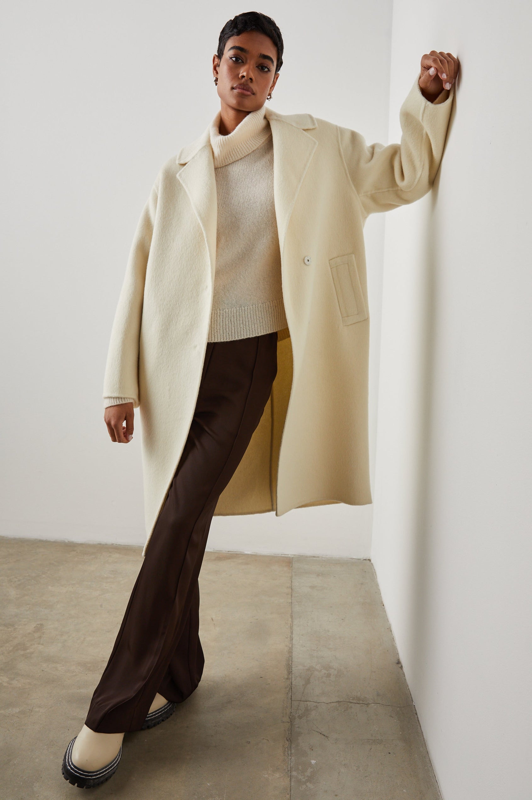 Lore Knee-Length Coat with Two Button Closure, Notched Lapels and Two Front Pockets in Ivory Colorway - Front Full Body View Featured on Model