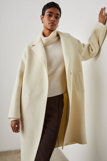 Lore Knee-Length Coat with Two Button Closure, Notched Lapels and Two Front Pockets in Ivory Colorway - Front View Featured on Model