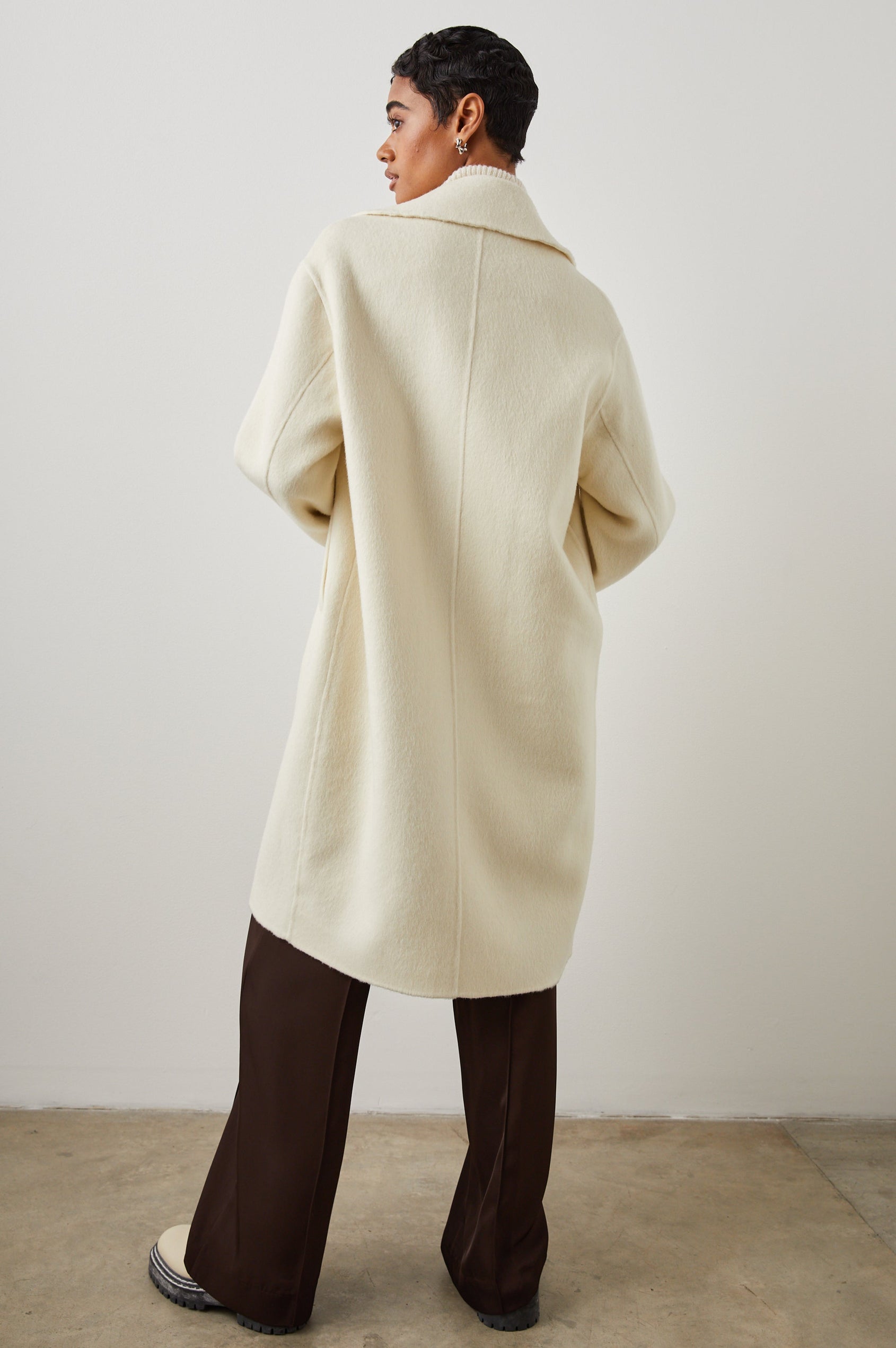 Lore Knee-Length Coat with Two Button Closure, Notched Lapels and Two Front Pockets in Ivory Colorway - Back Full Body View Featured on Model