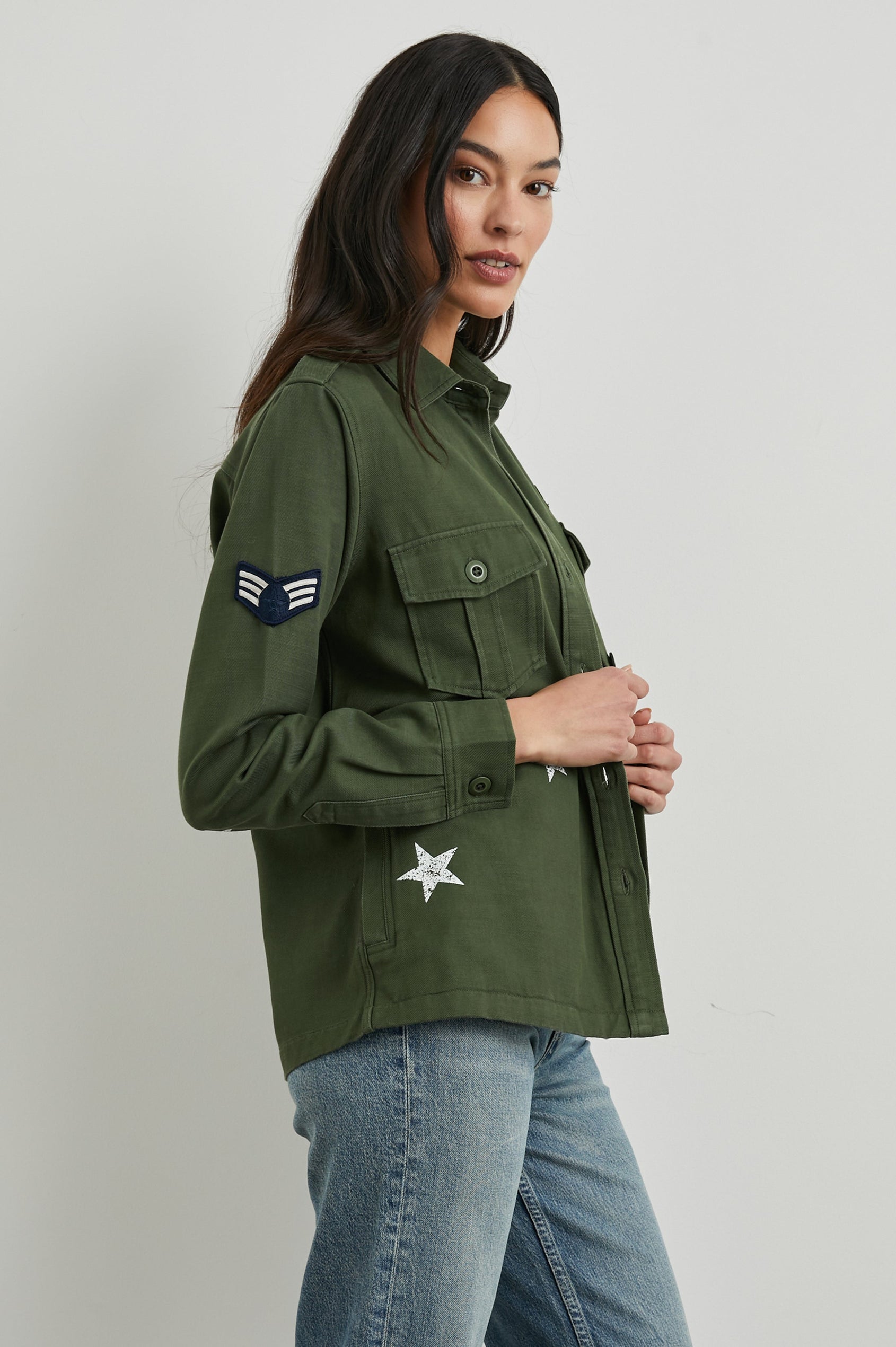Loren Long-Sleeve Shirt Jacket with Button Closure, Two Chest Button Flap Pockets, a Military Patch on Each Arm, a Military Number above One Chest Pocket, and Button Shoulder Tabs in Military Olive Colorway, with White Stars - Side View Featured on Model
