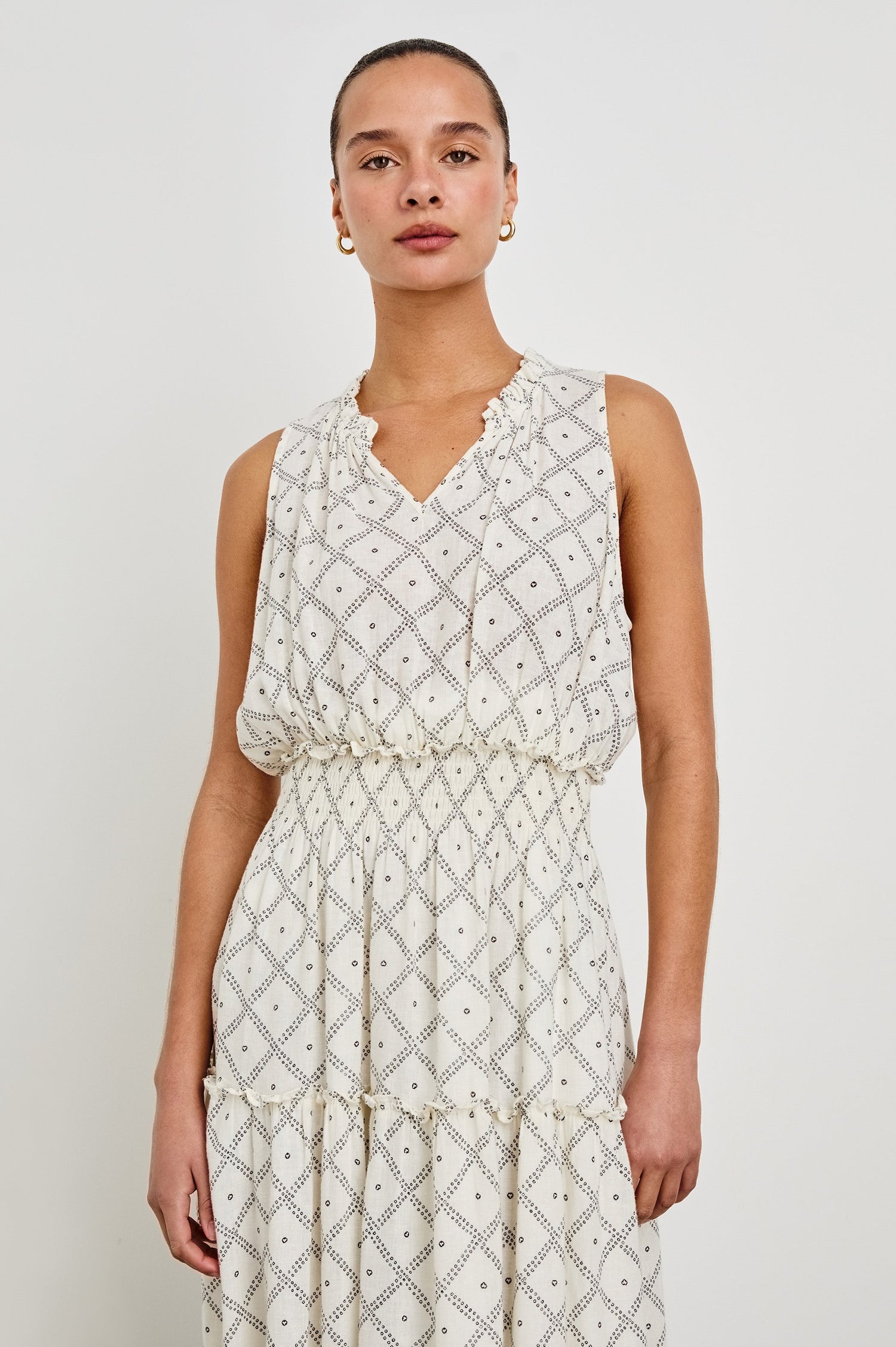 Female model is wearing the Loulou Maxi Dress in a black and white boho print. Dress is Ivory with black printed details. Features smocking at the waist, a v-neckline and fully-lined skirt with ruffle detail at each tier.