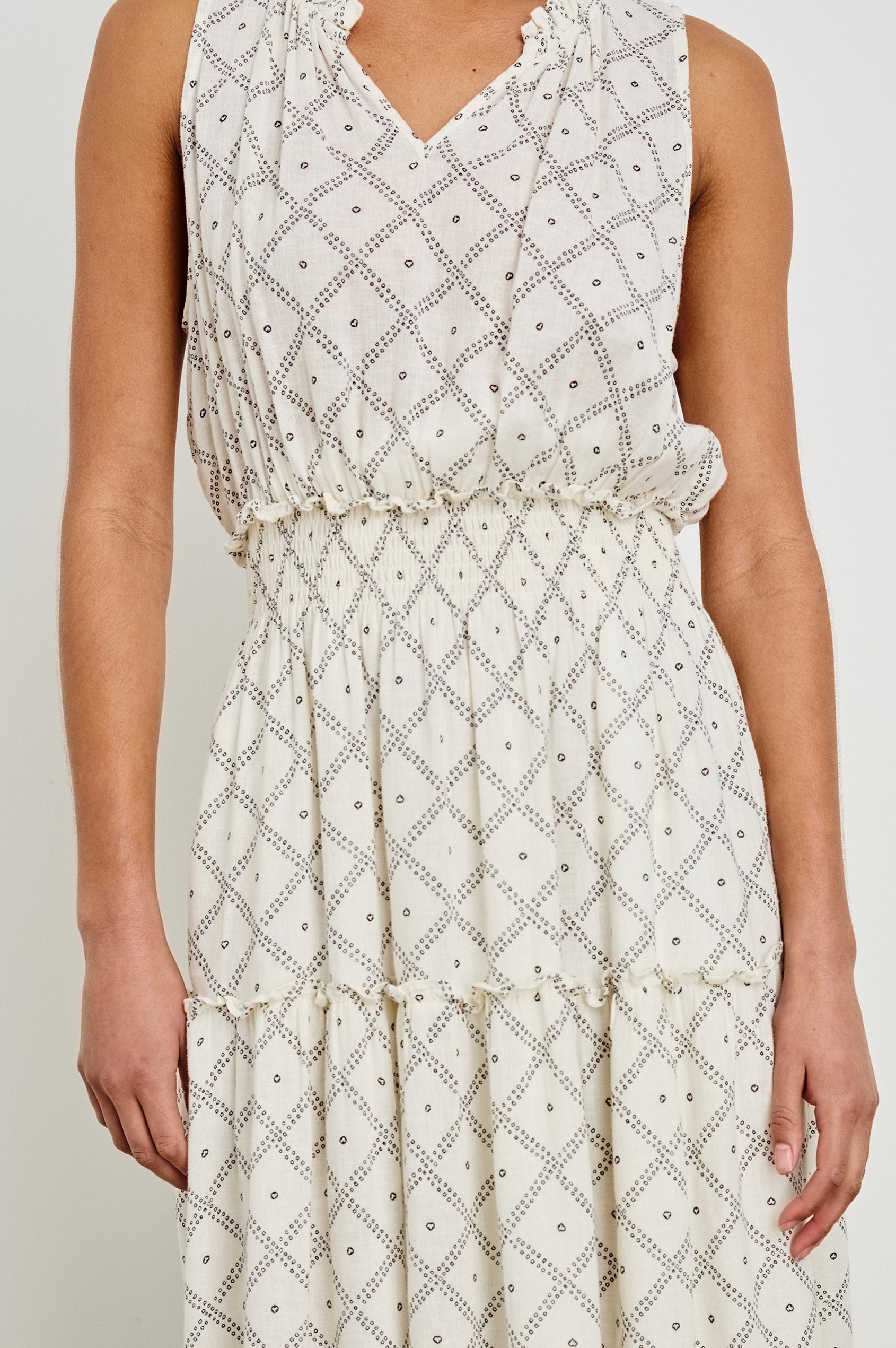 Female model is wearing the Loulou Maxi Dress in a black and white boho print. Dress is Ivory with black printed details. Features smocking at the waist, a v-neckline and fully-lined skirt with ruffle detail at each tier.