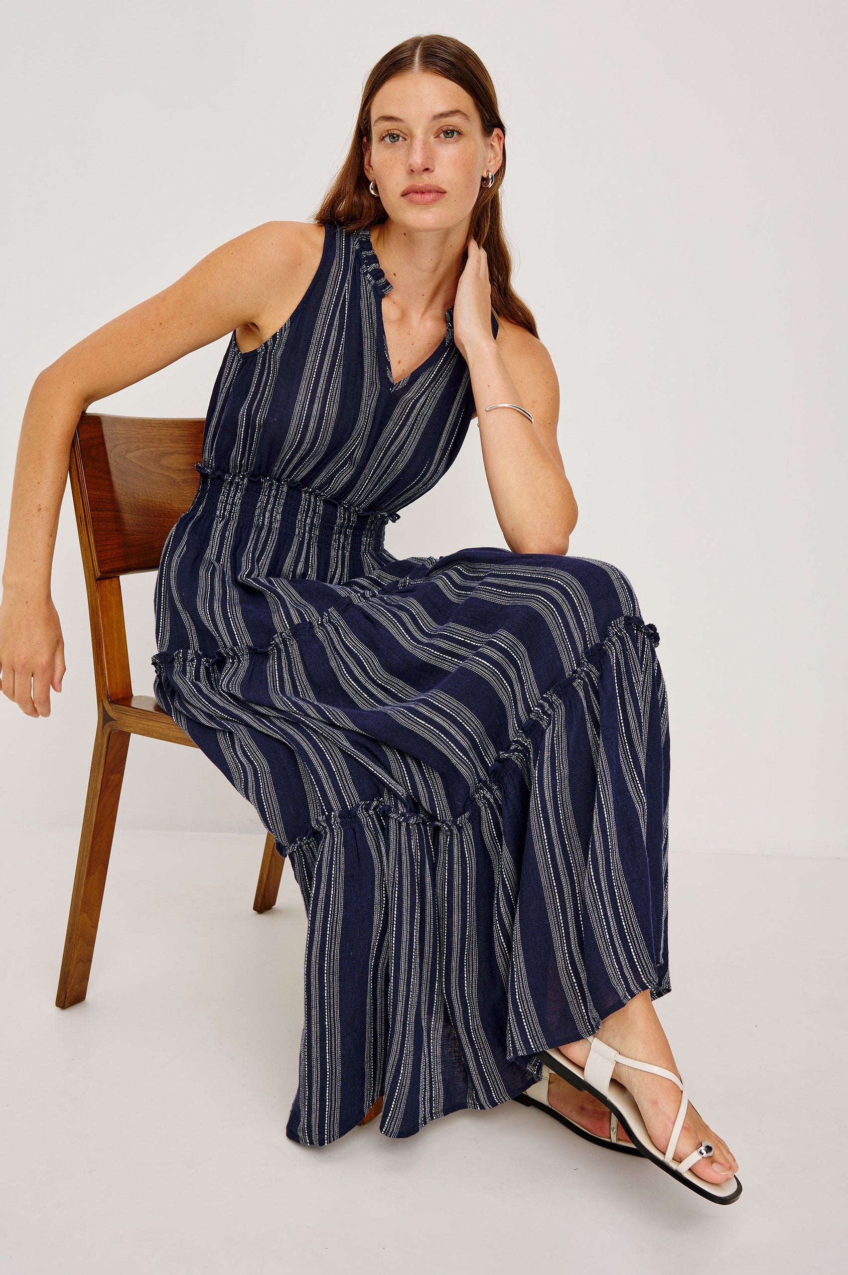 Loulou V-Neck Midi Dress with Smocked Elastic Waistband and a Multi Tiered Skirt in navy blue Magalia Stripe Colorway. Front view featured on model sitting in chair
