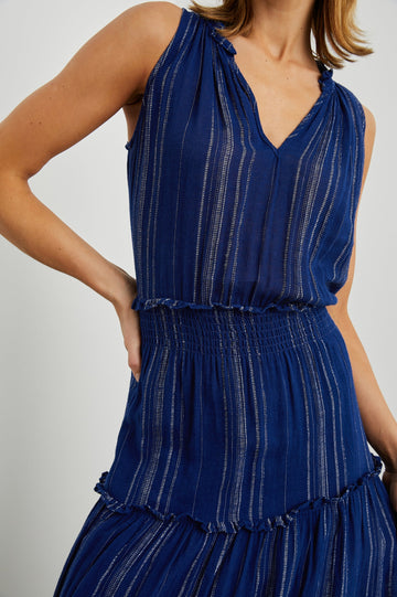 Loulou Sleeveless Midi Dress with a V Neck, Shirred Collar, Smocked Waist and Tiered Skirt in Nola Stripe Colorway, Thin White Vertical Stripes on dark blue - Front View Featured on Model