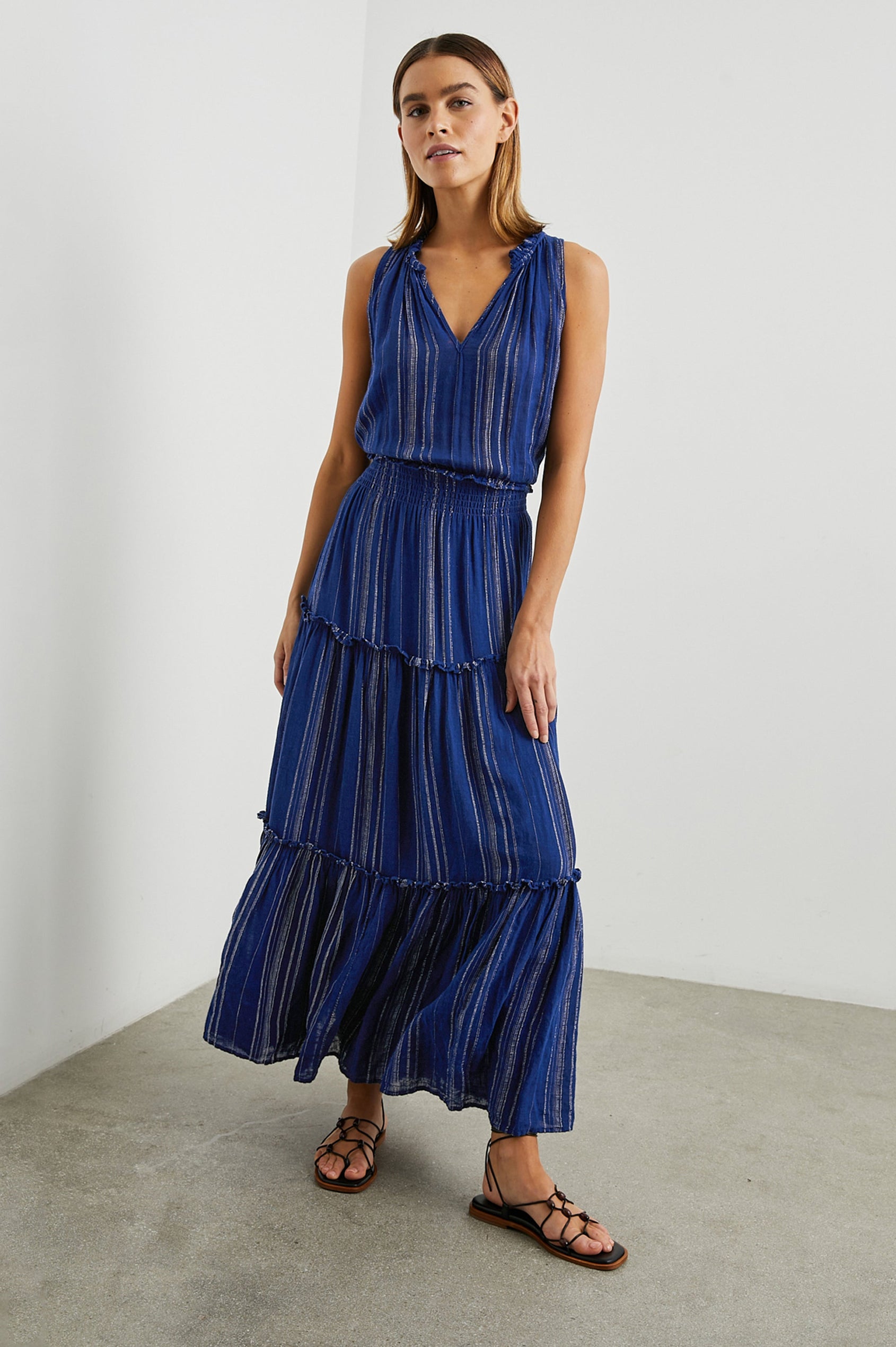 Loulou Sleeveless Midi Dress with a V Neck, Shirred Collar, Smocked Waist and Tiered Skirt in Nola Stripe Colorway, Thin White Vertical Stripes on dark blue - Front Full Body View Featured on Model