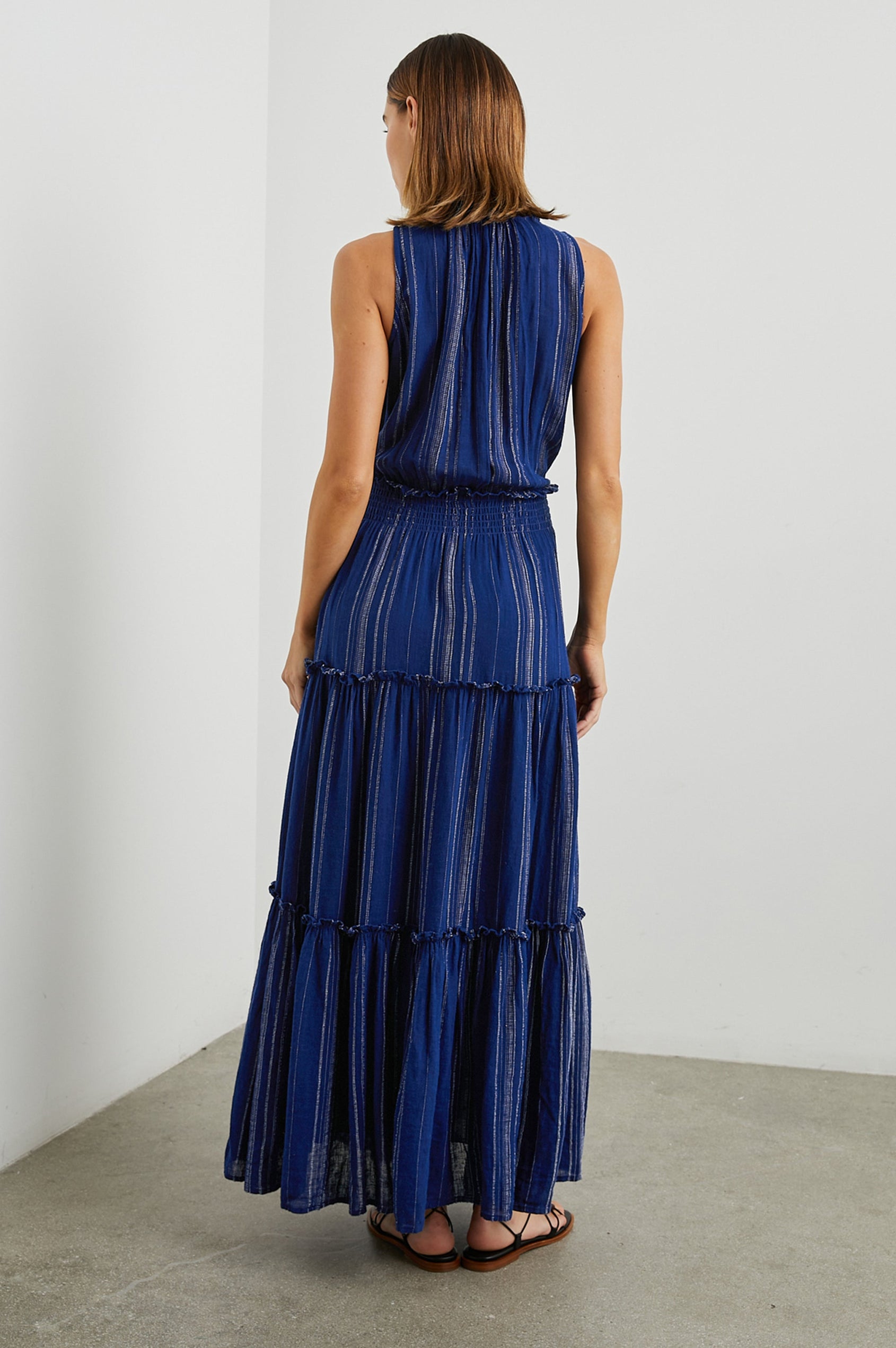 Loulou Sleeveless Midi Dress with a V Neck, Shirred Collar, Smocked Waist and Tiered Skirt in Nola Stripe Colorway, Thin White Vertical Stripes on dark blue - Back Full Body View Featured on Model