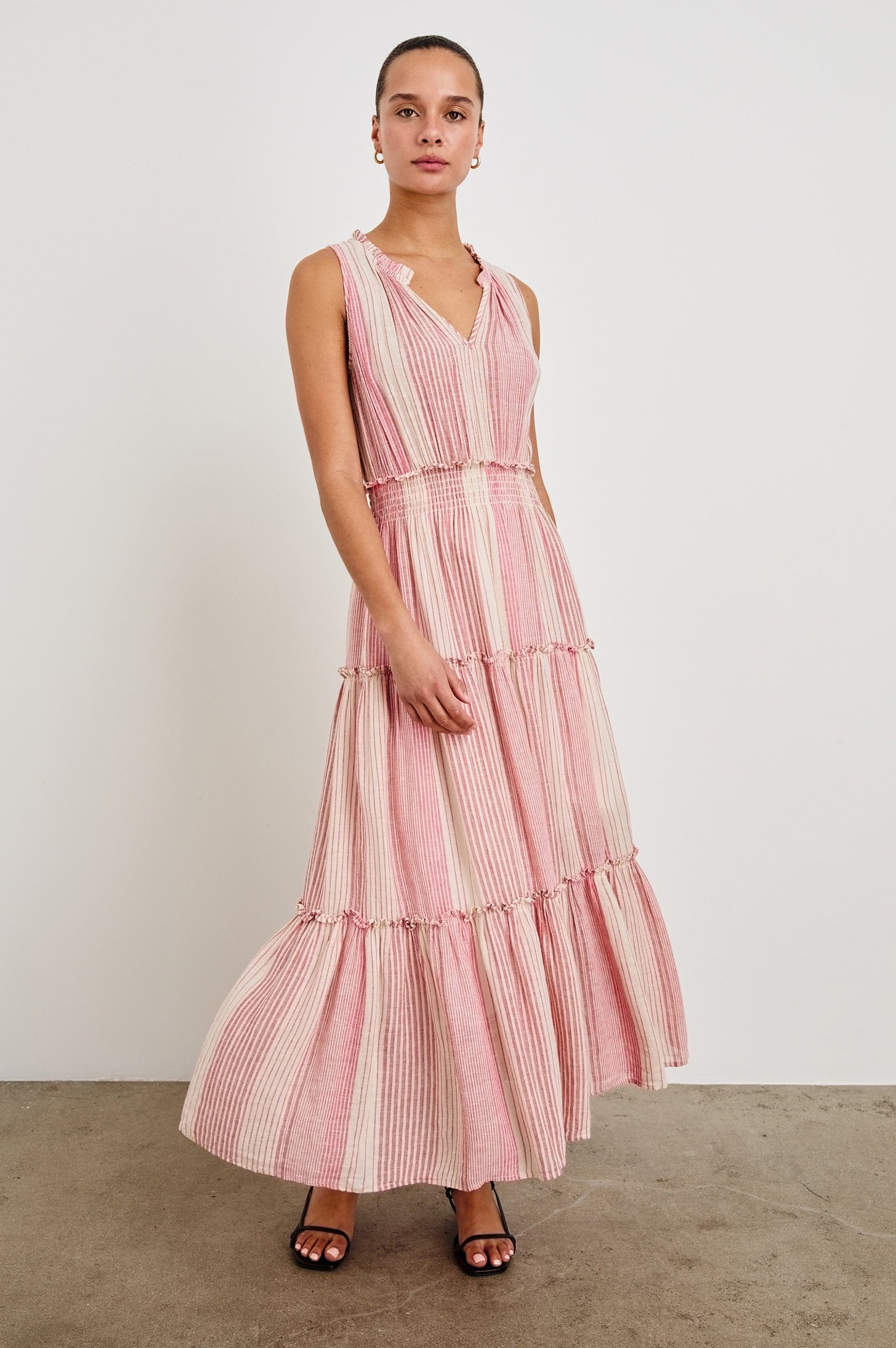 Front view of female model wearing our sleeveless, Loulou Maxi Dress in color Salerno Stripe, a pink and white boho stripe. Dress features smocked waist, v-neck, and tiered maxi skirt. 