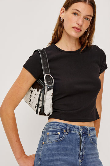The Lucca is a long-hair cowhide shoulder bag with an adjustable strap and polished silver oval buckle. In Cowgirl Haircalf colorway. Side view modeled on the shoulder featured.