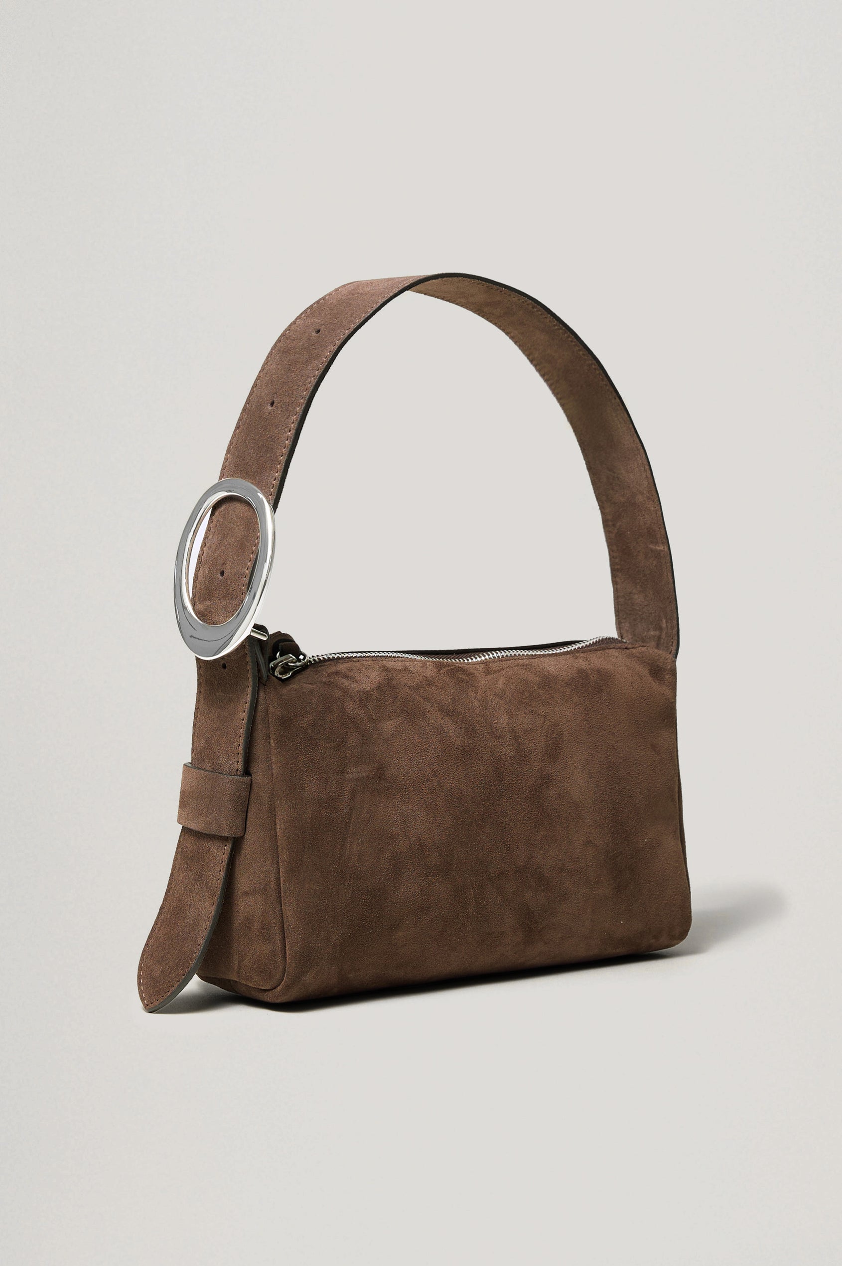 The Lucca is a smooth suede shoulder bag with an adjustable strap and polished silver oval buckle. In Espresso Suede colorway. Front angeled view featured.