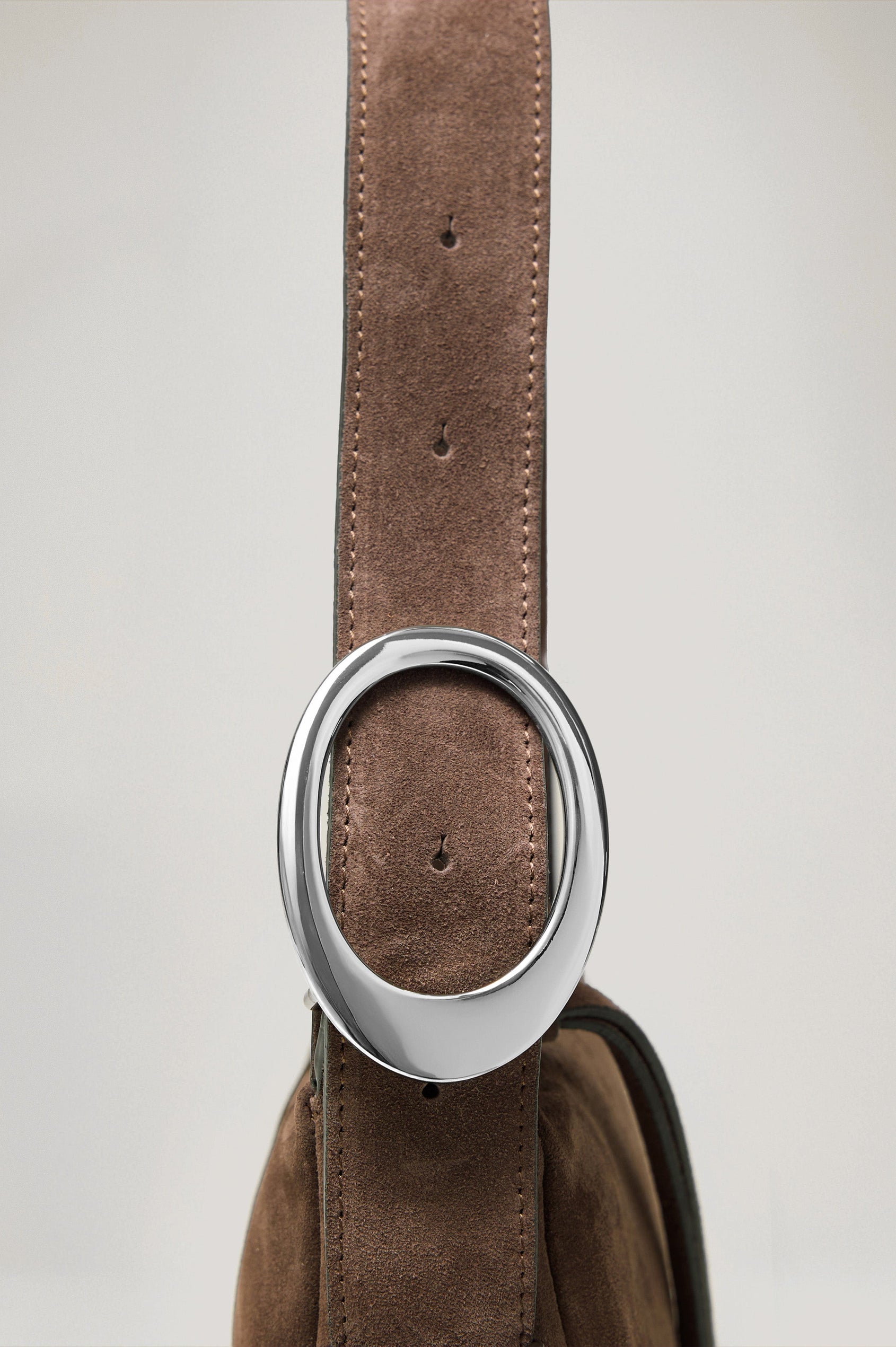 The Lucca is a smooth suede shoulder bag with an adjustable strap and polished silver oval buckle. In Espresso Suede colorway. Close up view of strap featured.