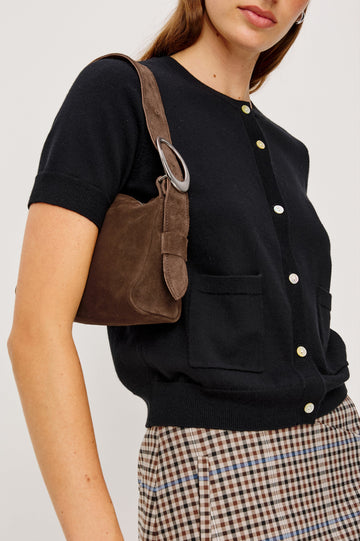 The Lucca is a smooth suede shoulder bag with an adjustable strap and polished silver oval buckle. In Espresso Suede colorway. Side view on the model's shoulder featured.