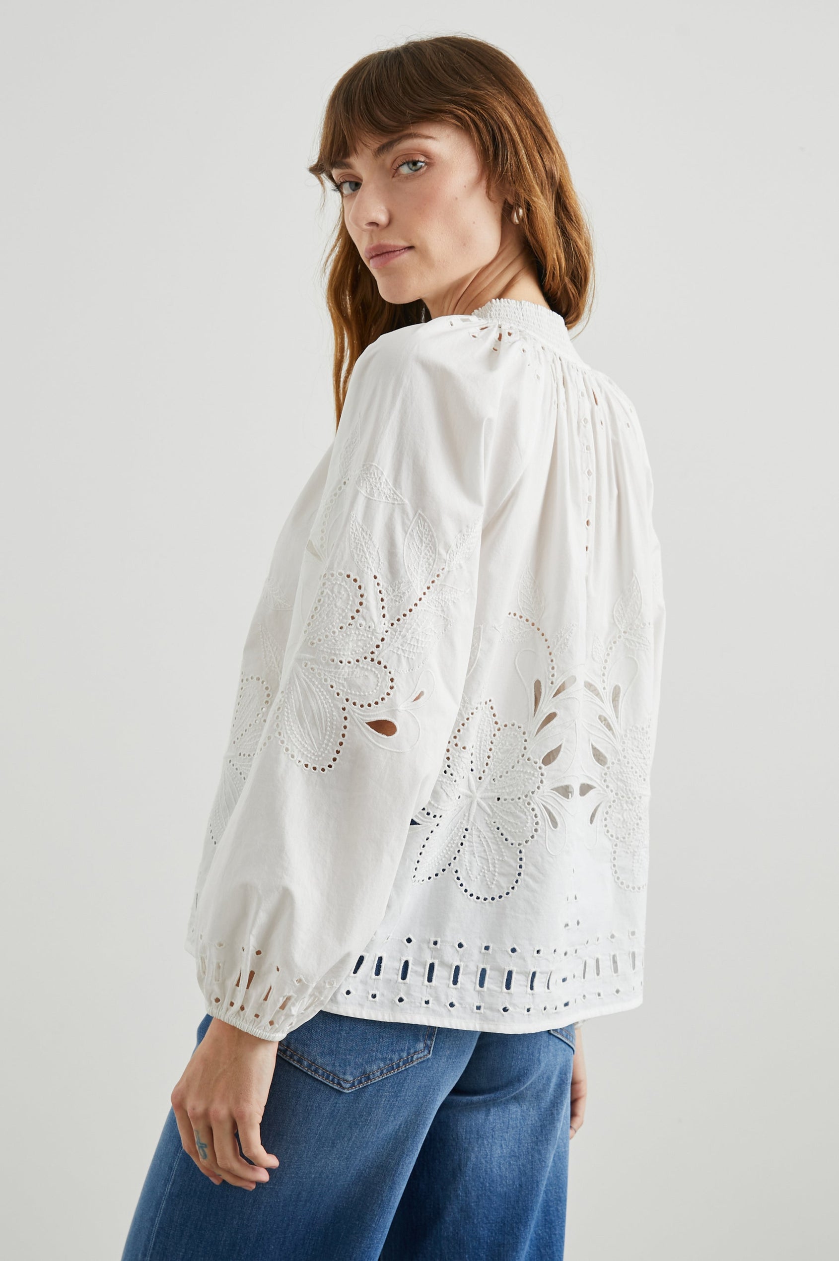 Lucinda Long-Sleeve Top with Billowy Sleeves, a V Neck with a Drawstring Collar, and a Floral and Geometric Eyelet Design in White Colorway - Side View Featured on Model  