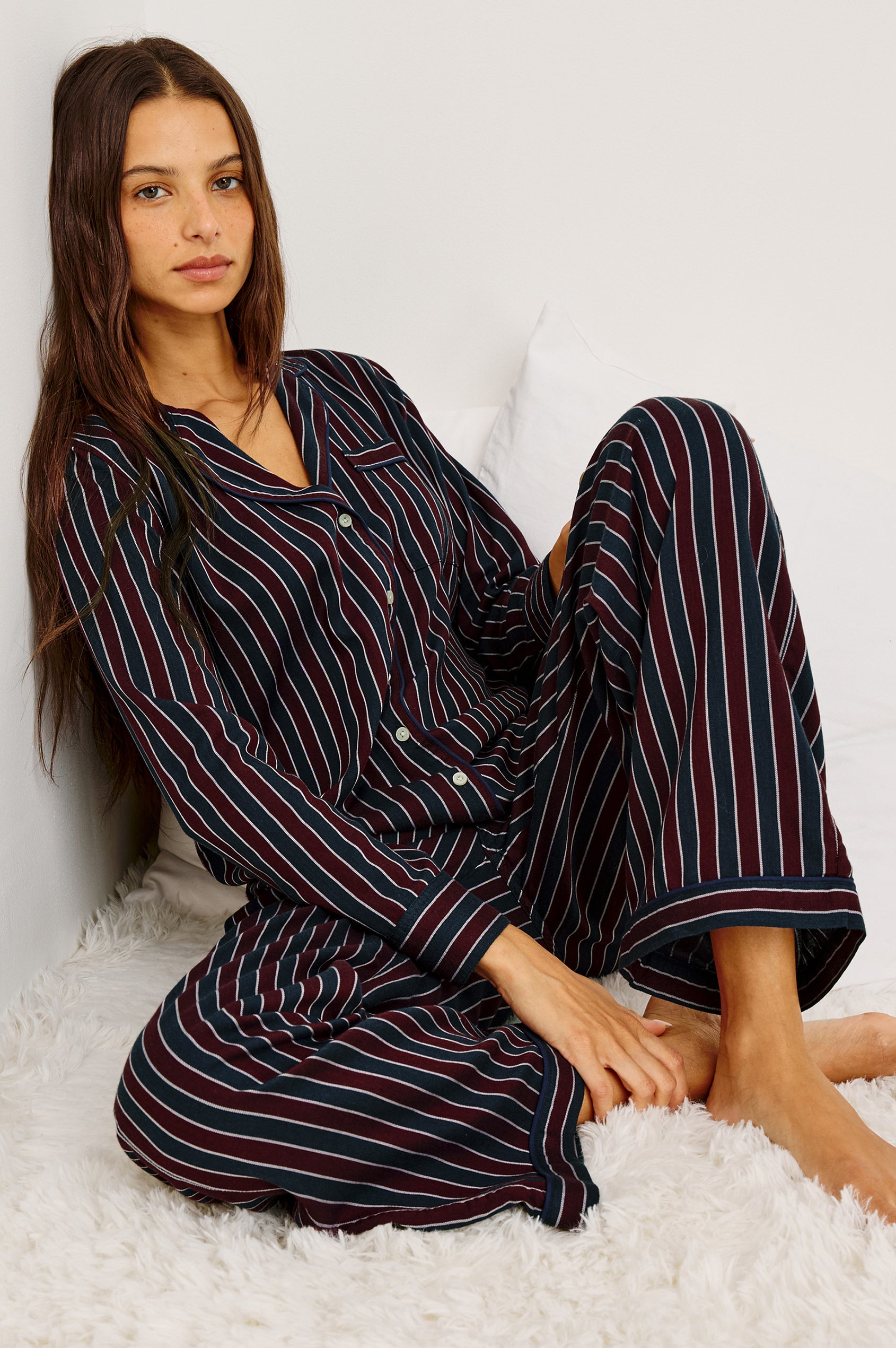 Luna Pajama Set in Signature Rayon With Button-Up Collared Shirt With Front Buttons, Long Sleeves, Chest Patch Pocket and Matching Pant With Side Pockets and Drawstring Waist Ties in Navy Oxblood Stripe Colorway - Full Body Front View Featured on Model Sitting