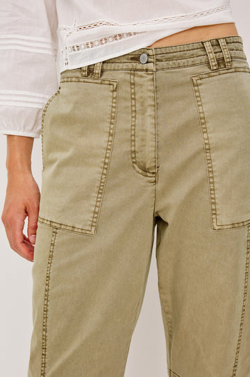 Mid-rise, barrel-leg pants made from stretch twill in Light Olive colorway. The pants have knee seaming, front pockets, a zip fly, and an adjustable drawstring waist for a casual, comfortable fit. Close up of details on model.