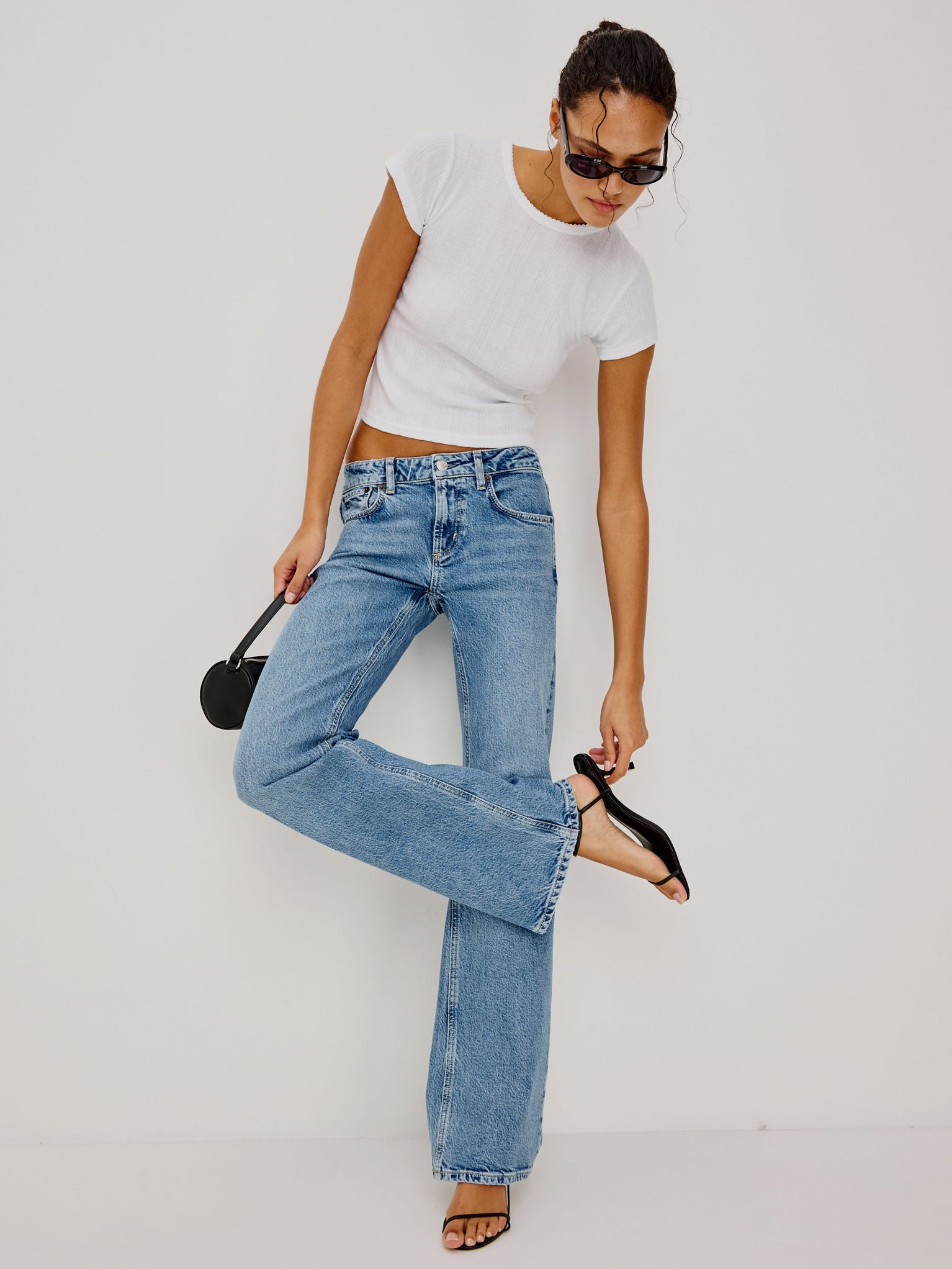 Woman wearing light blue jeans and a white t-shirt on a plain background