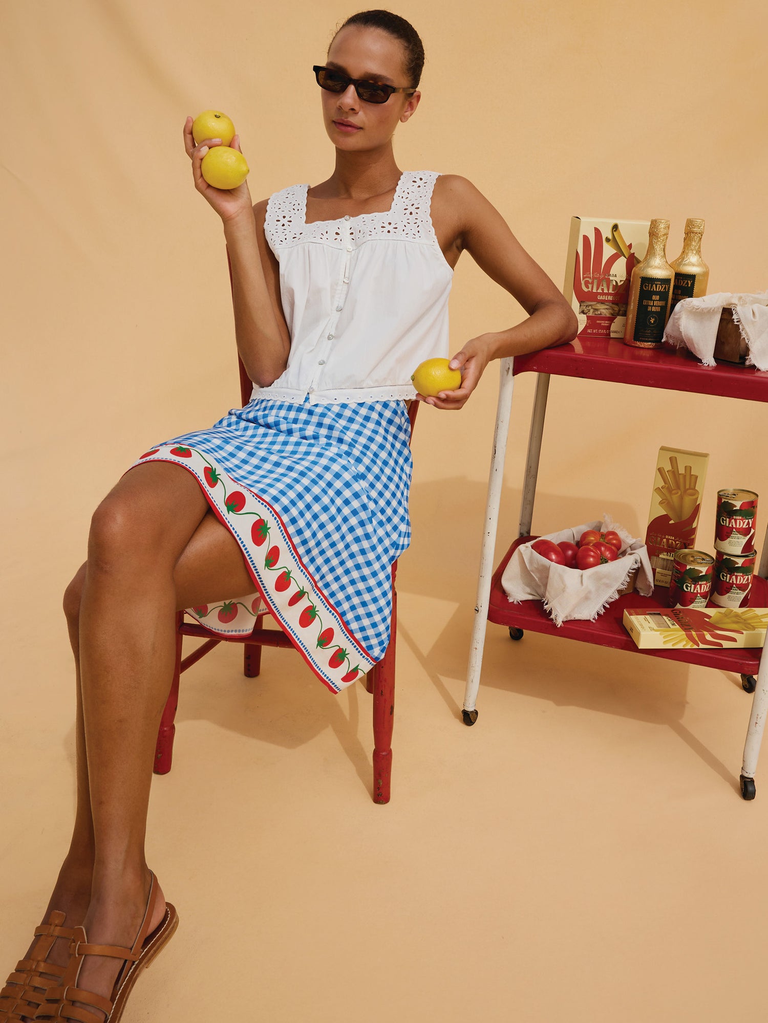 Woman in a white top and blue checkered skirt holding lemons against a beige background