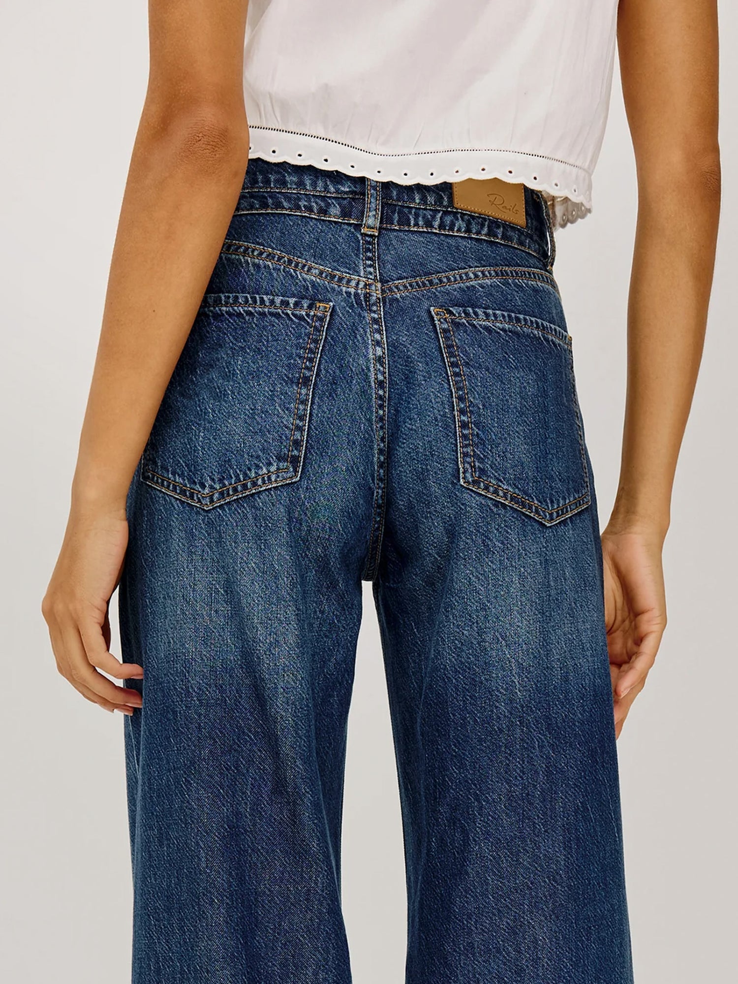 Person wearing blue jeans and a white top on a plain background