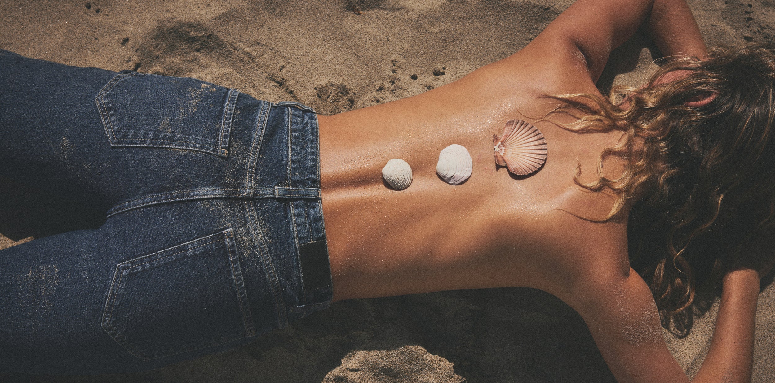 Person lying on sand with seashells and a shell pendant