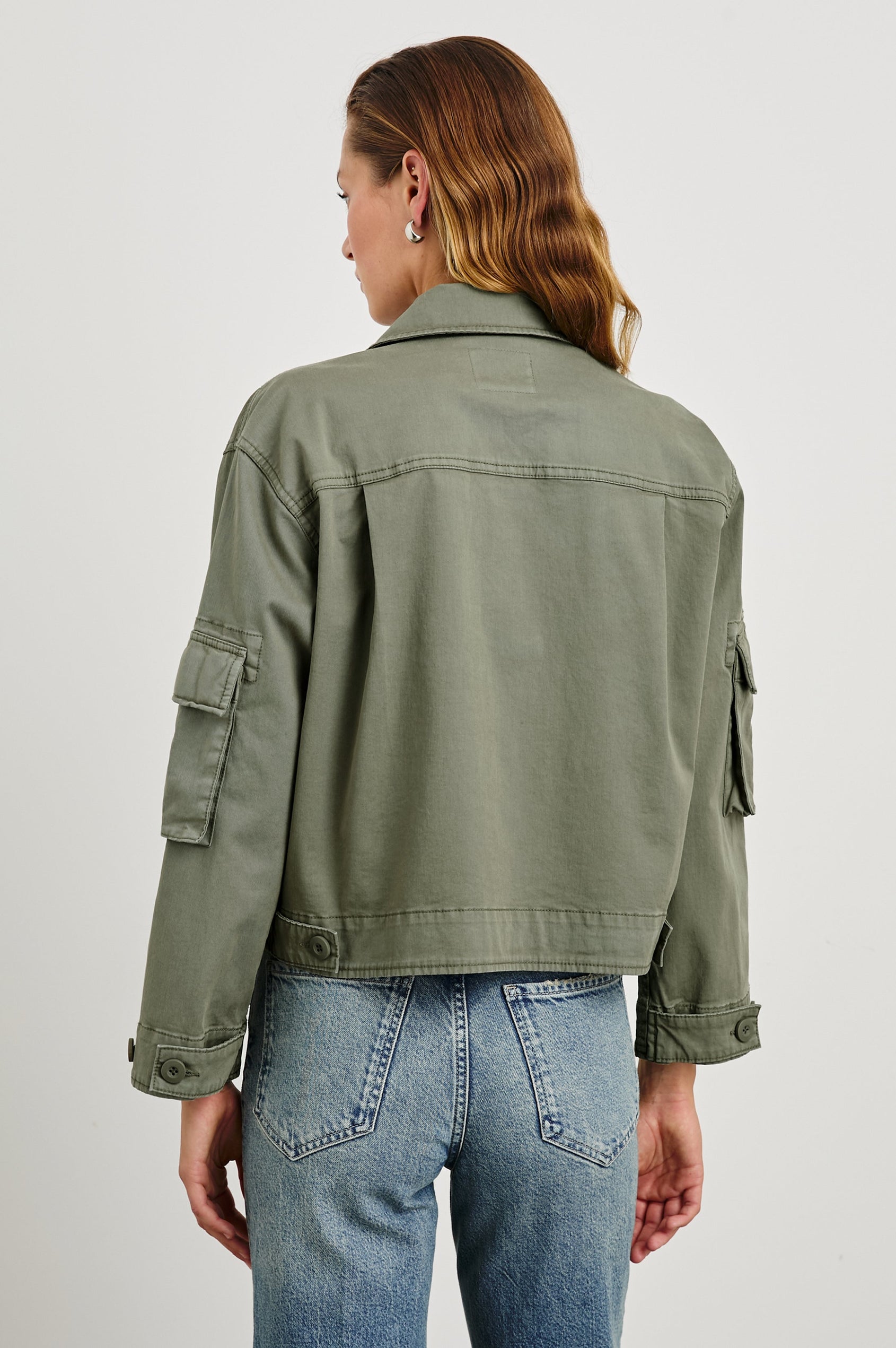 Madison Jacket with Button Closure, Two Chest Flap Pockets, Two Sleeve Flap Pockets, Adjustable Button Tab at Cuffs, and a Button Tab at Hem in Dark Olive Colorway - Back View Featured on Model  