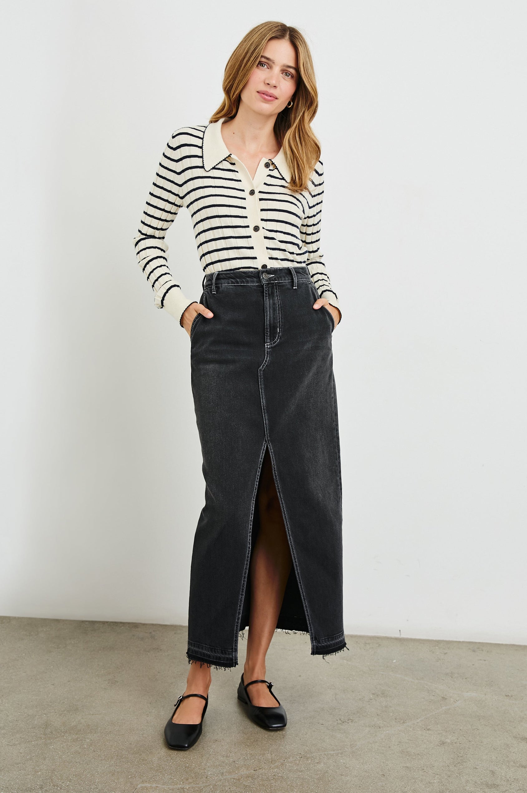 Manhattan Midi Denim Skirt with a Raw Hem, a Front Center Thigh Slit, Belt Loops, Two Front Pockets and Two Back Patch Pockets in Eclipse Colorway, a Black - Front Full Body View Featured on Model