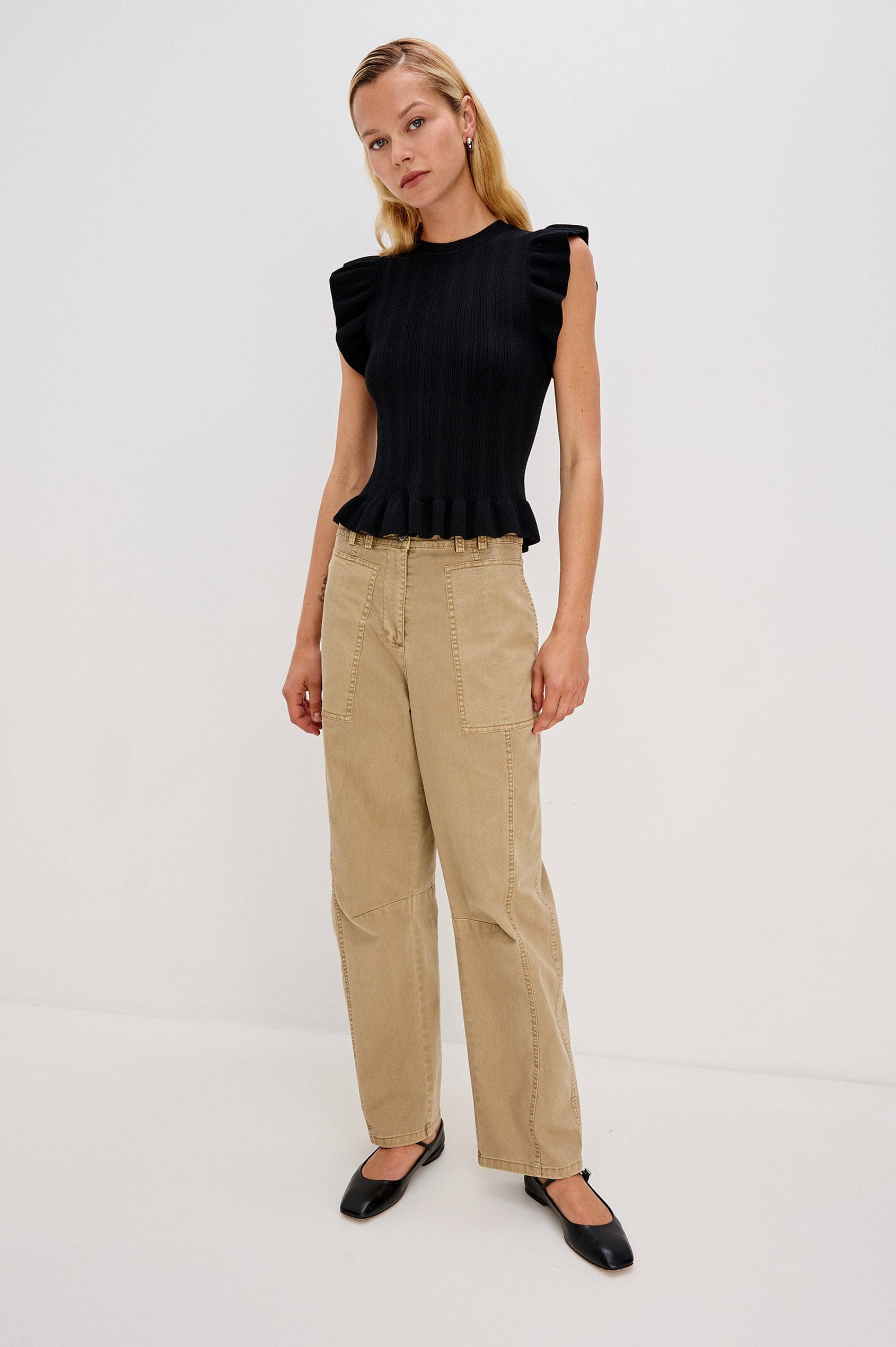 Marci is a short-sleeve fine-gauge knit sweater top. The fitted silhouette is accented with flutter sleeves and a ruffled hem in Black Colorway - Full Body Front View Featured on Model