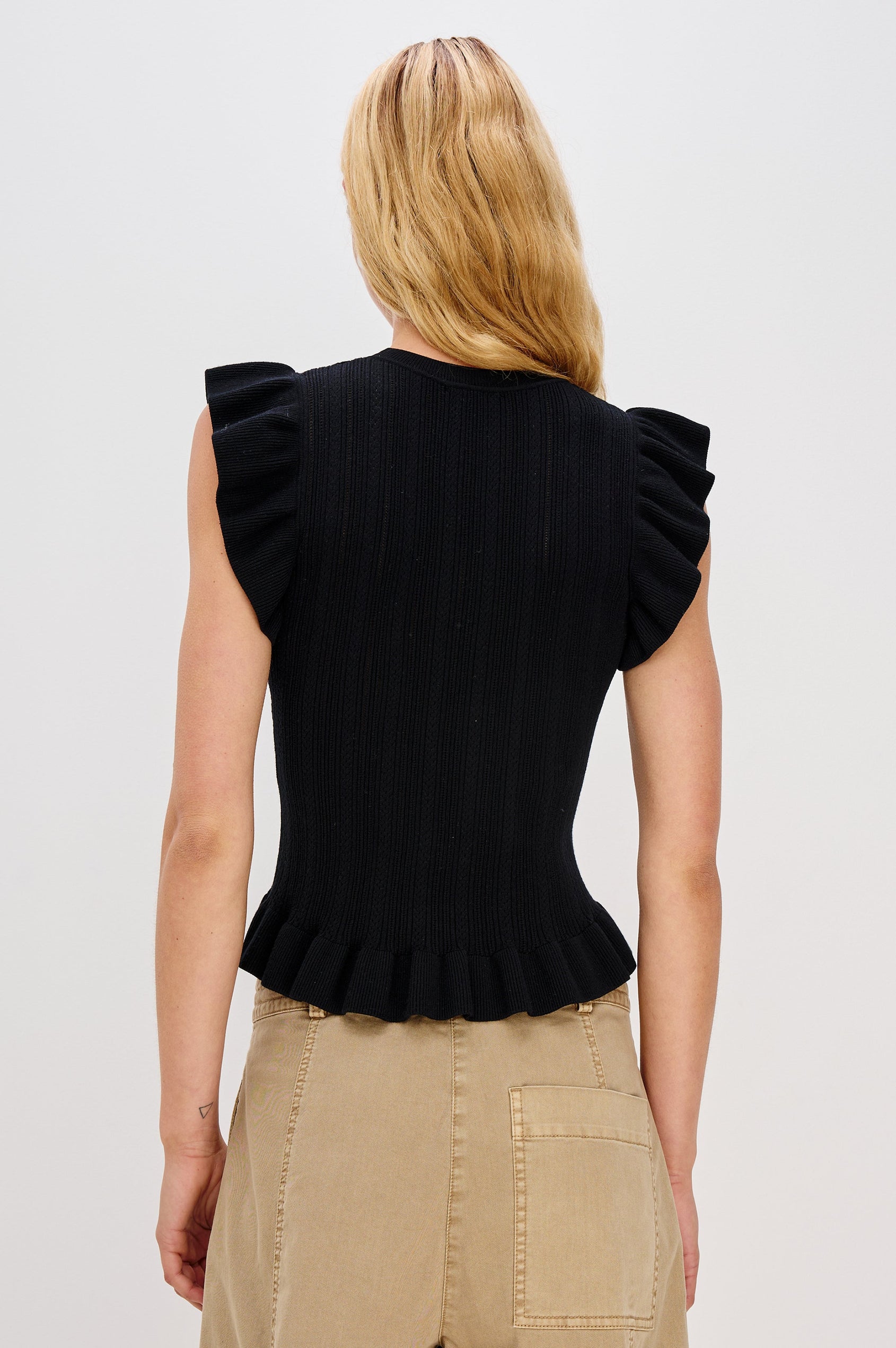 Marci is a short-sleeve fine-gauge knit sweater top. The fitted silhouette is accented with flutter sleeves and a ruffled hem in Black Colorway - Back View Featured on Model